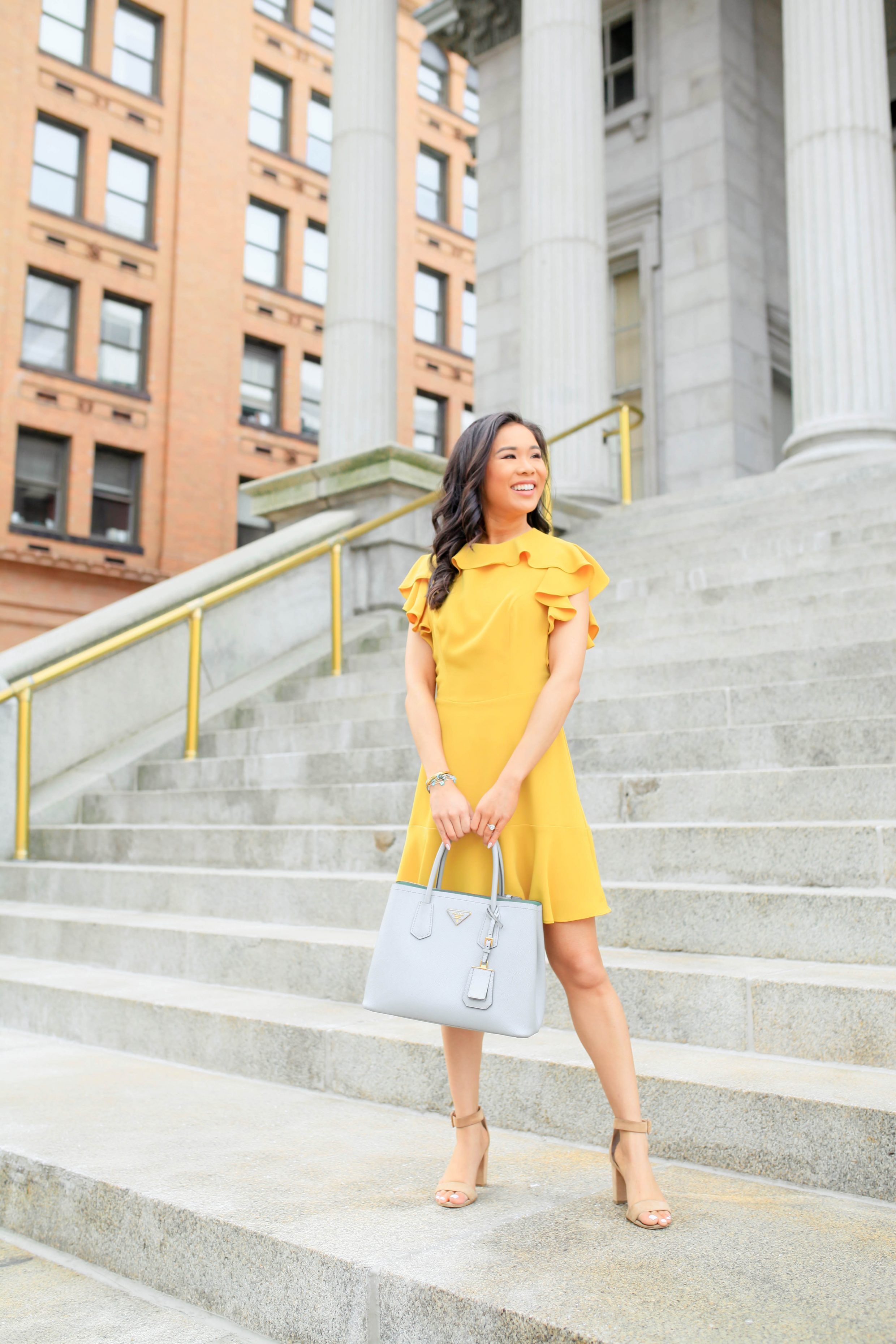 Hoang-Kim wears a marigold ruffle dress with suede block heels and Prada Cuir tote