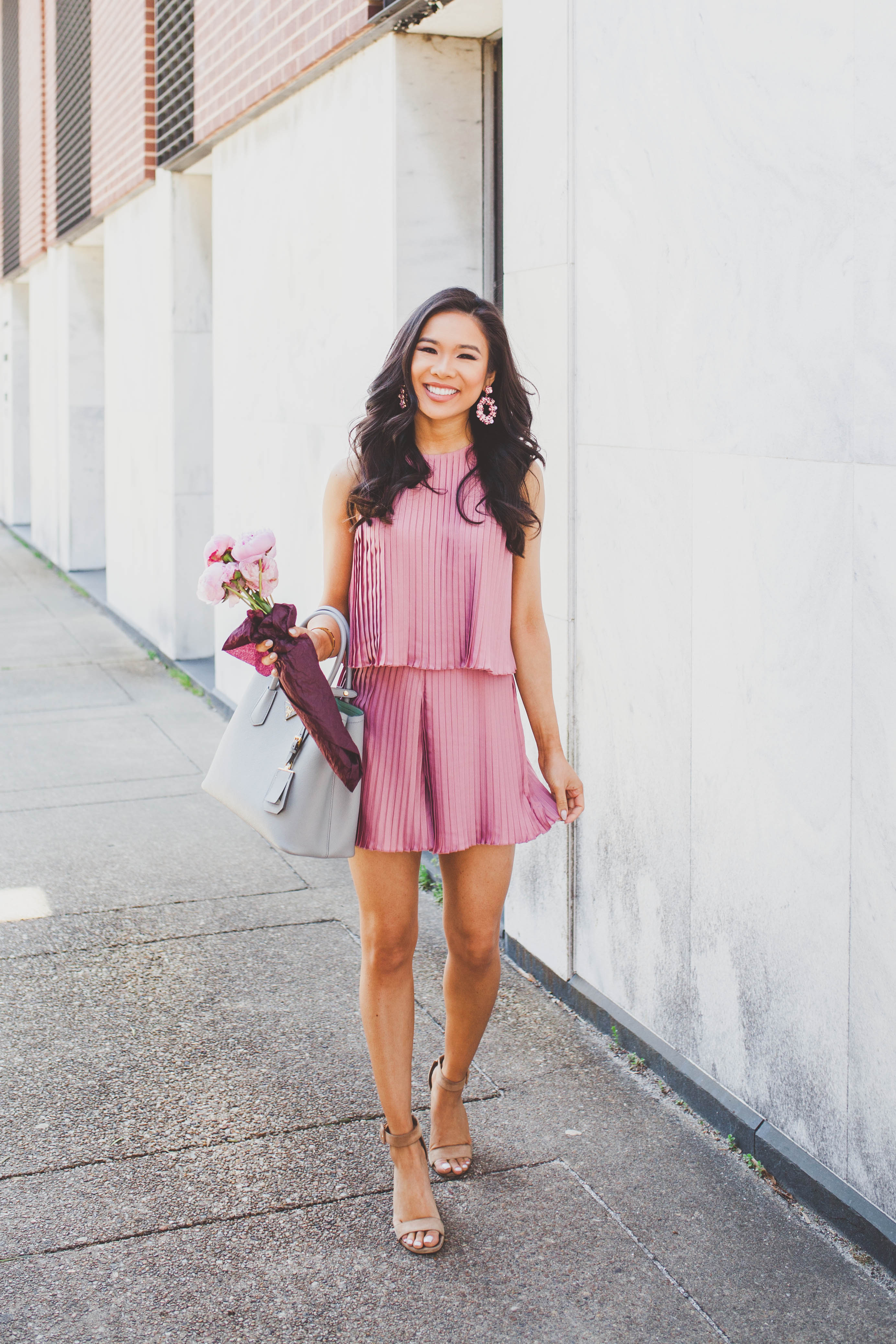 Blogger Hoang-Kim wears a pink pleated romper with suede block sandals and pink peonies