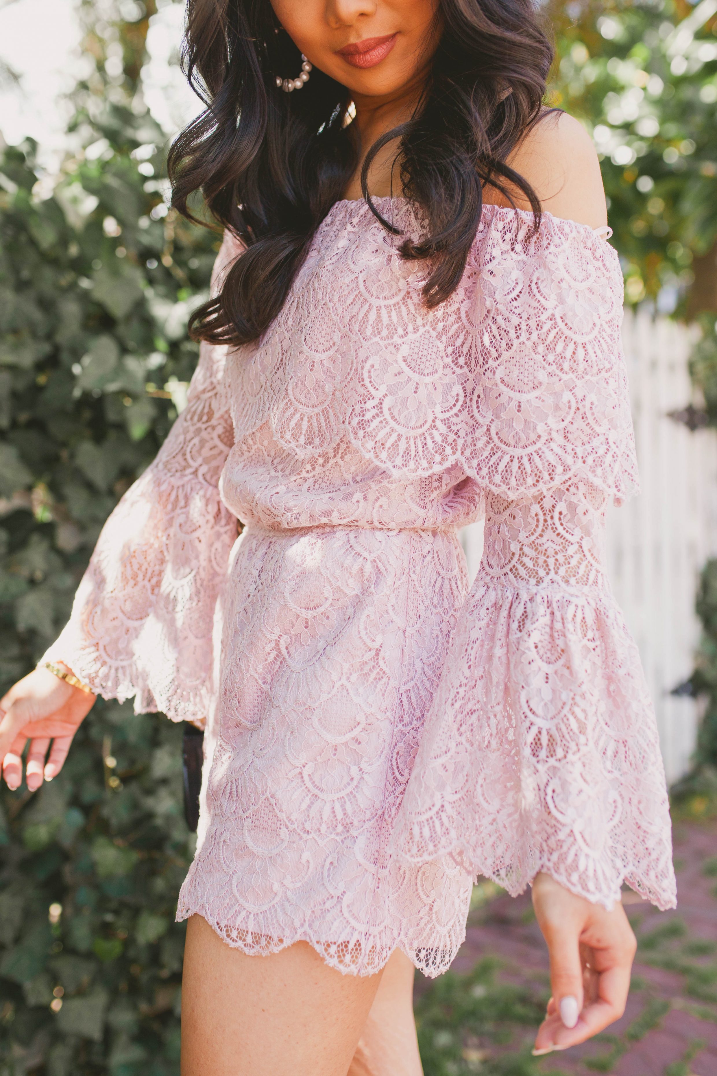 Hoang-Kim wears a blush lace off-the-shoulder romper with pearl hoop earrings