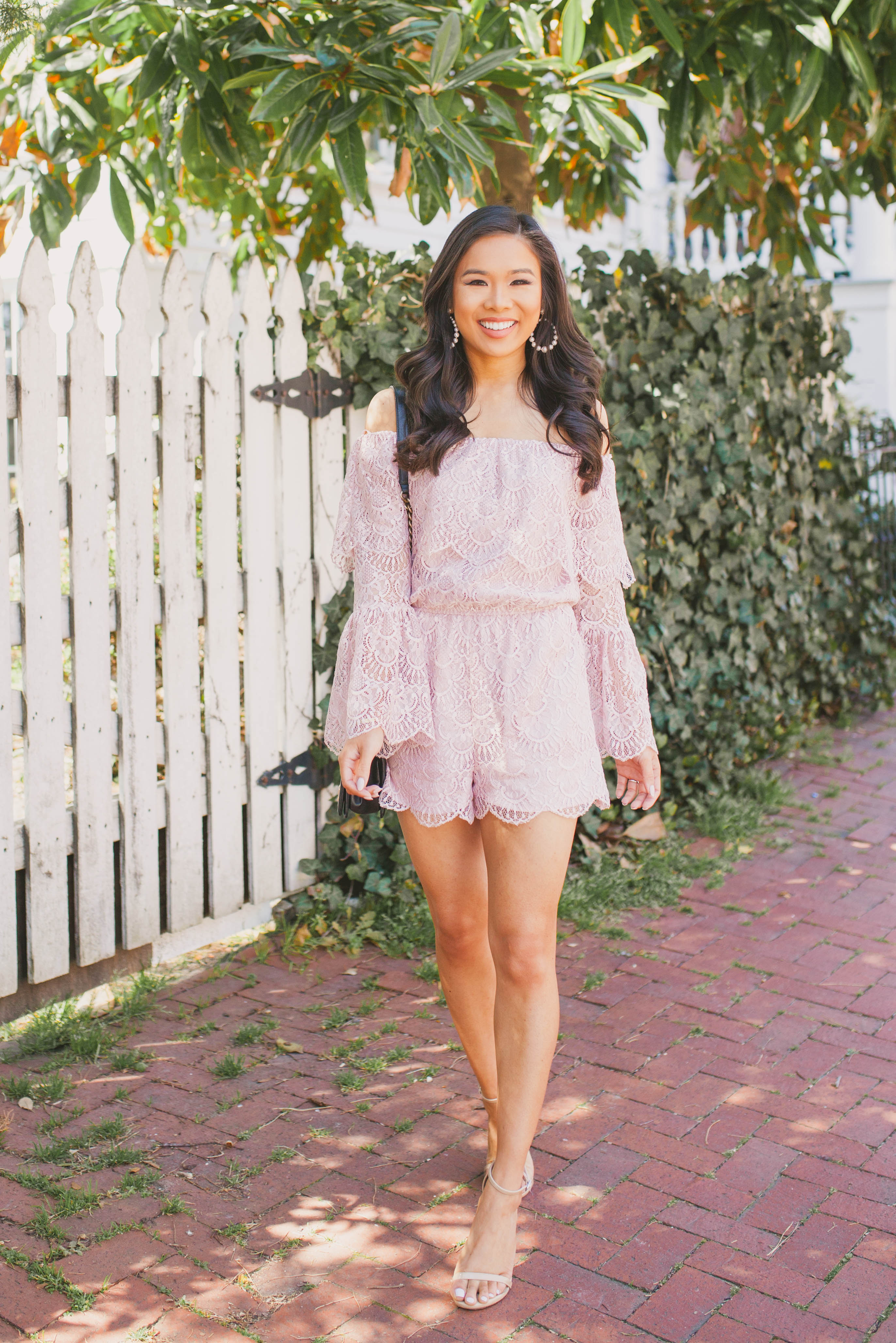 Hoang-Kim wears a blush lace off-the-shoulder romper with pearl hoop earrings