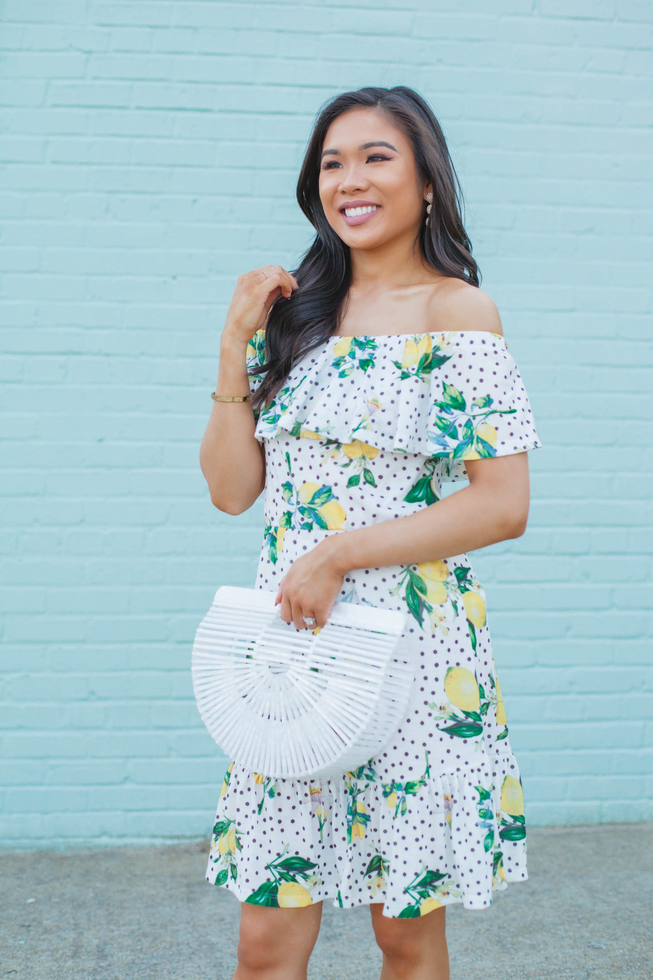 Hoang-Kim wears an off the shoulder lemon print dress with a white acrylic bag for summer