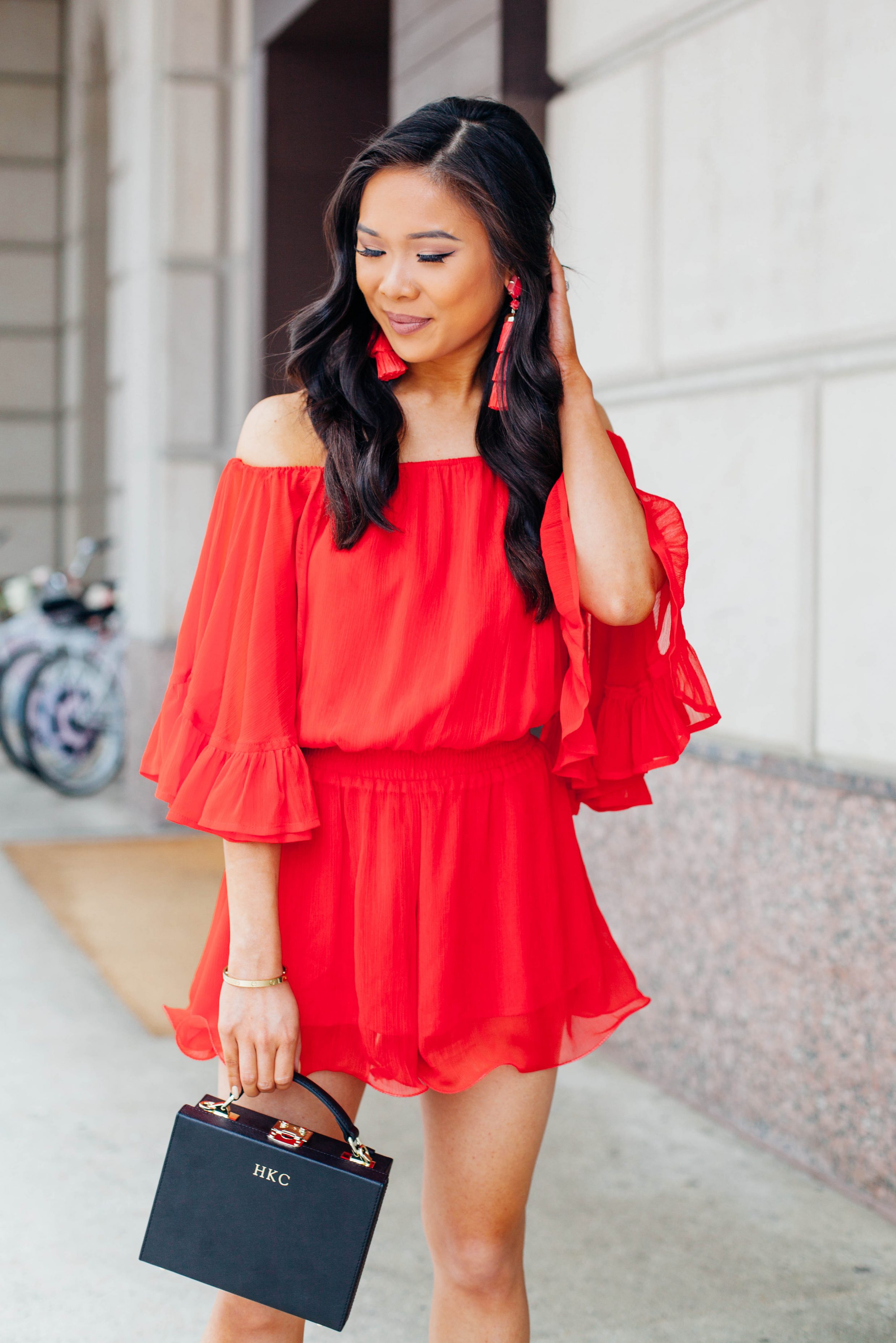Hoang-Kim wears a red off the shoulder romper with tassel earrings and black box bag