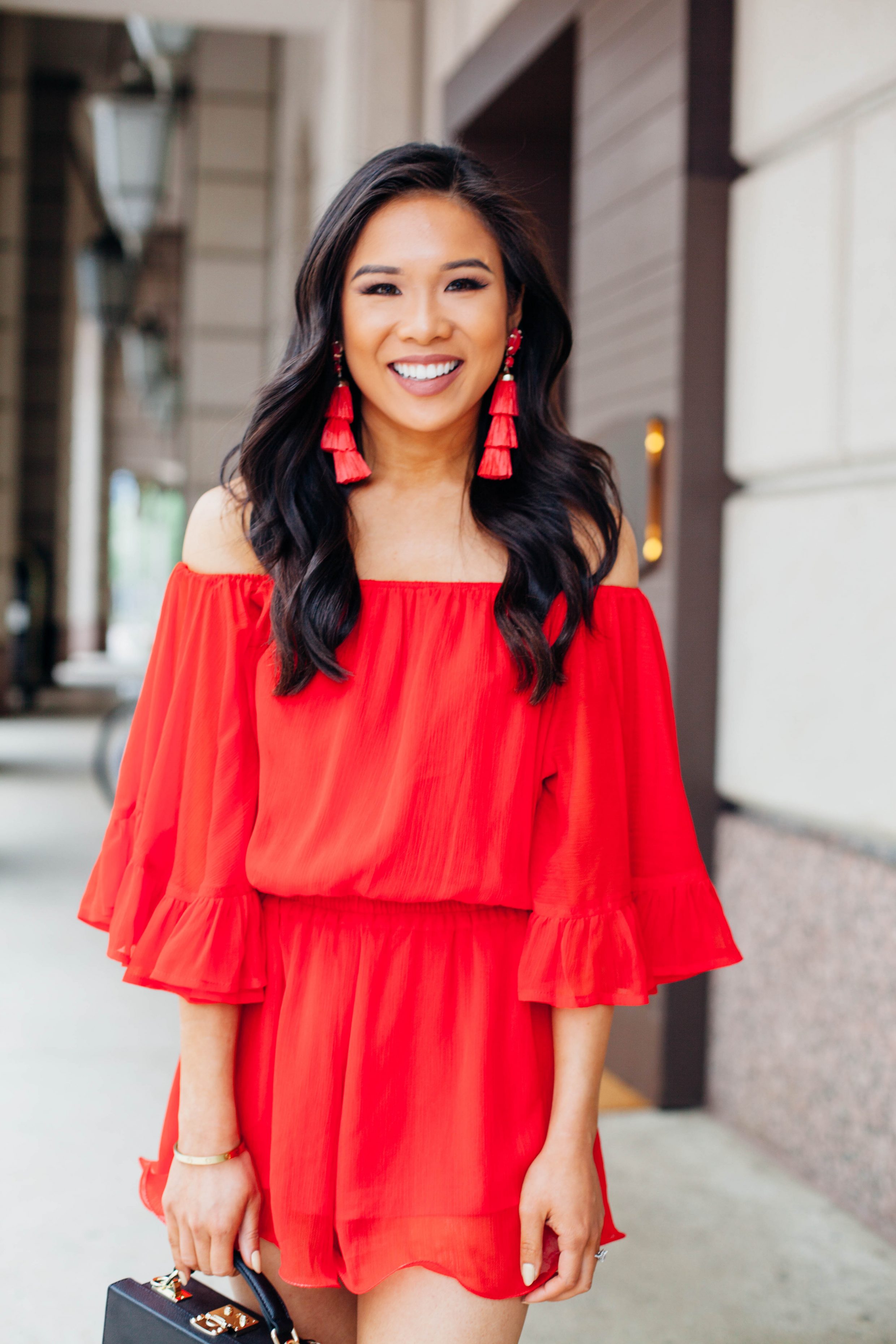 Hoang-Kim wears Kendra Scott Denise tassel earrings with a red off the shoulder romper and black box bag from The Daily Edited