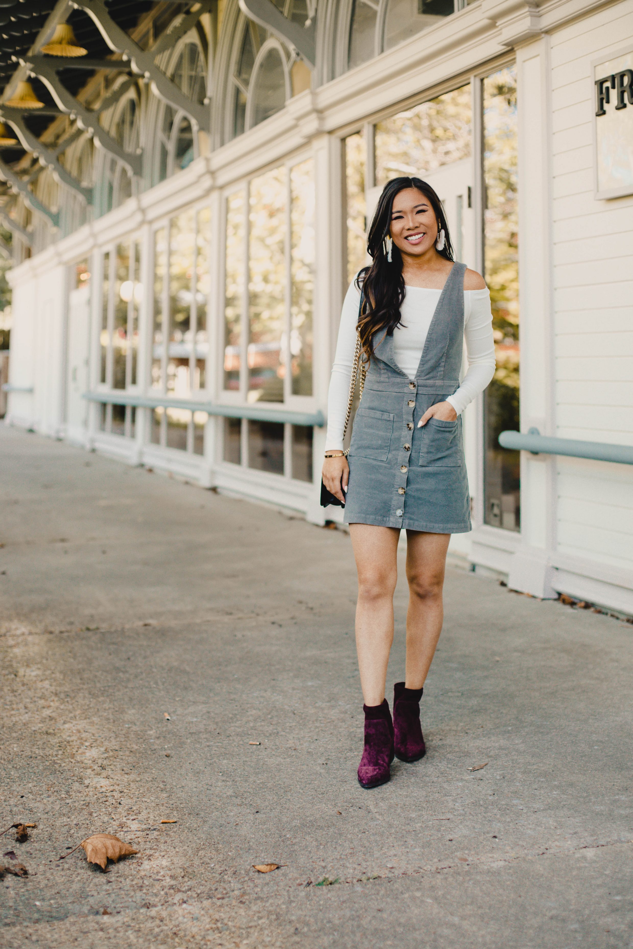 Blogger Hoang-Kim wears a corduroy overall dress with a white off-the-shoulder top for fall