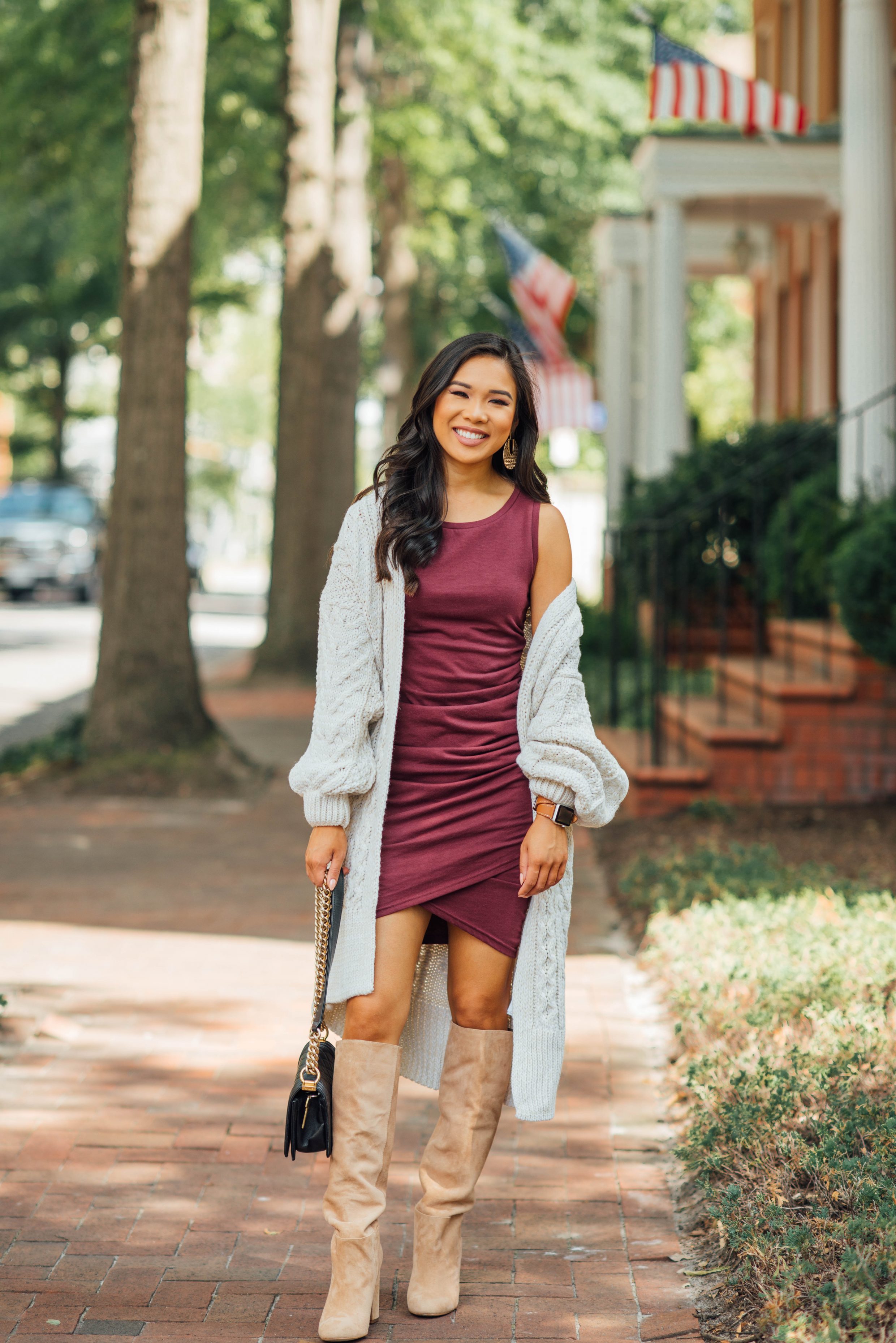 Blogger Hoang-Kim wears a burgundy dress, cream cardigan and knee high boots for fall
