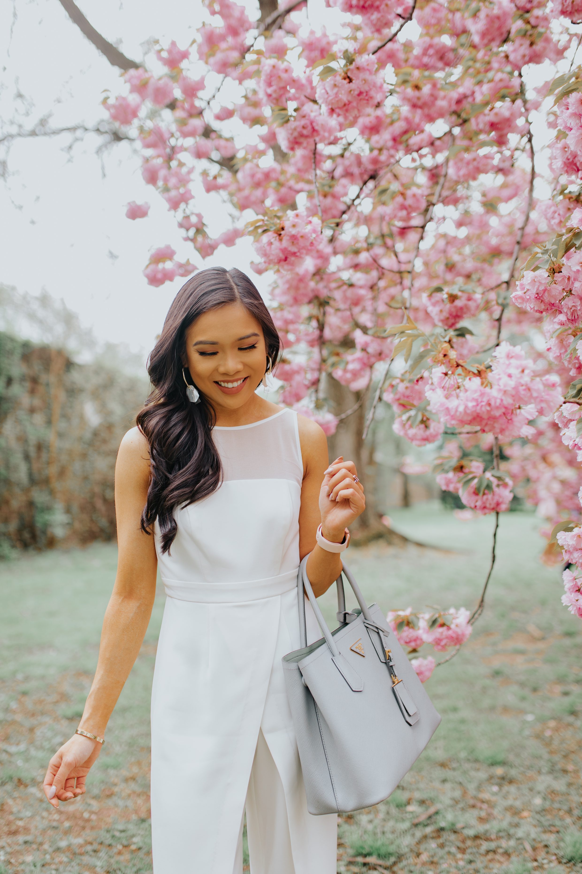 Brunette woman wears a white jumpsuit in front of cherry blossoms