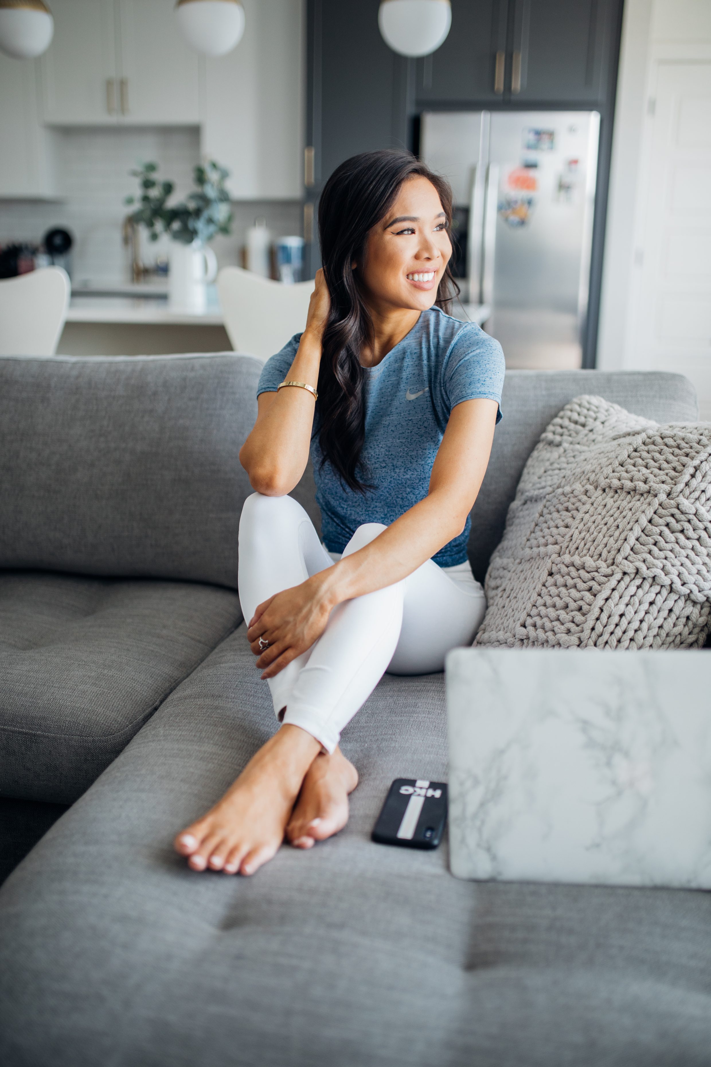 Petite blogger wearing activewear apparel on a gray sofa in her Dallas apartment with two toned cabinets
