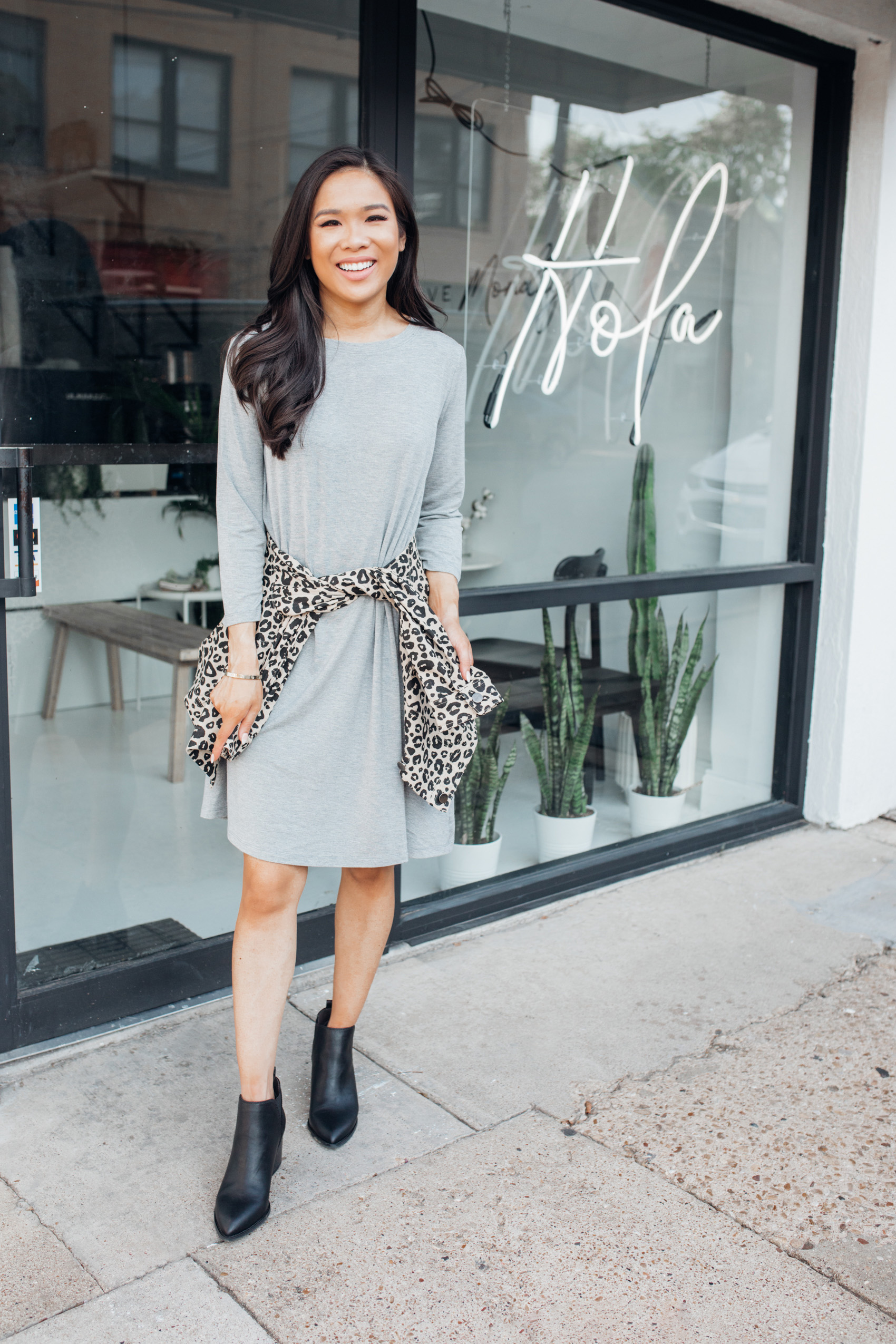 Blogger Hoang-Kim shares affordable fall fashion with Walmart wearing a gray shirt dress, leopard jacket and black booties for a fall outfit at Hola Cafe in Bishop Arts