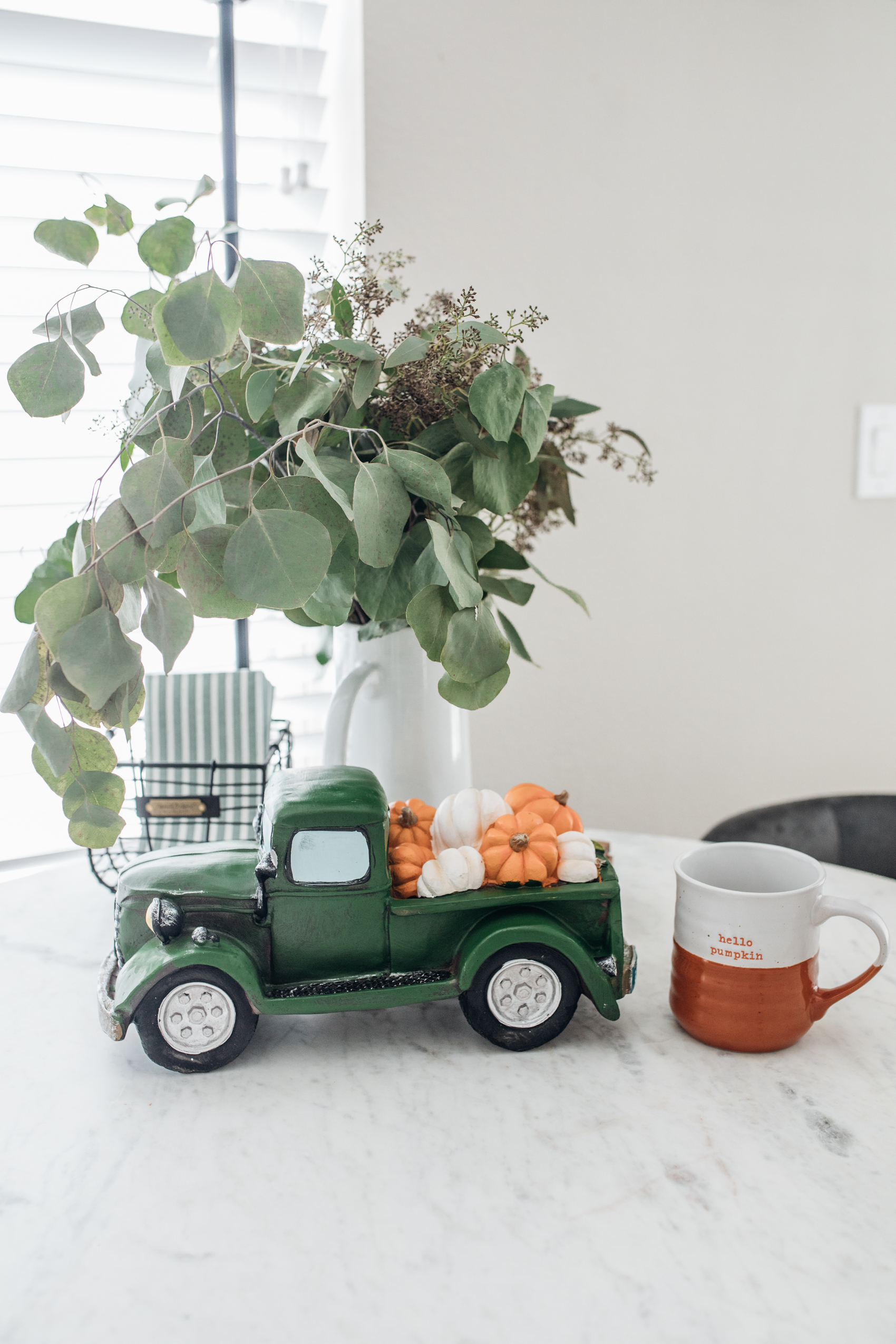 Fall kitchen table decor with green pickup truck, pumpkins and mug in Dallas apartment