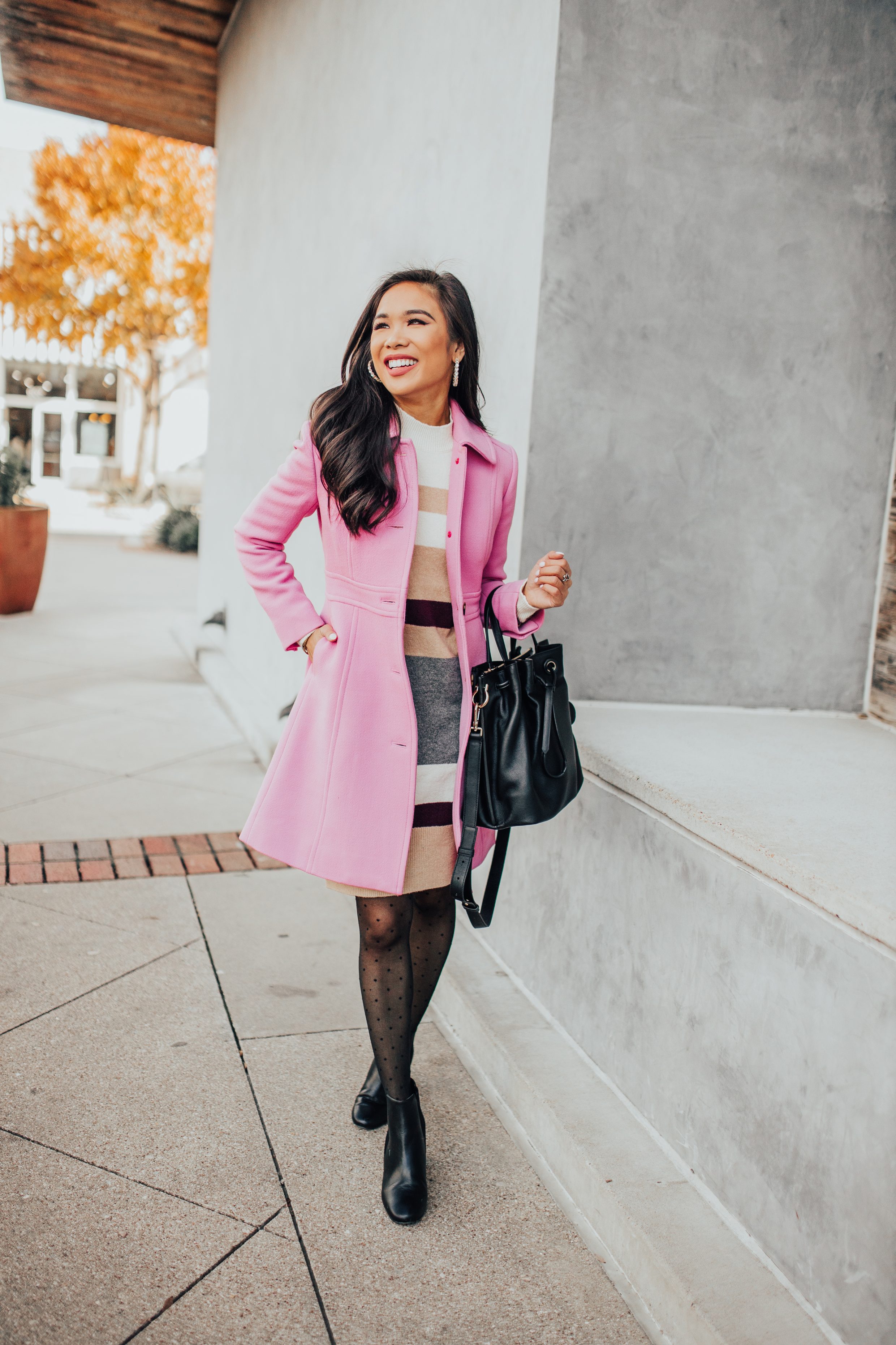 Pink winter coat over a striped mockneck sweater dress with polka dot tights, black booties and a bucket bag on petite blogger Hoang-Kim