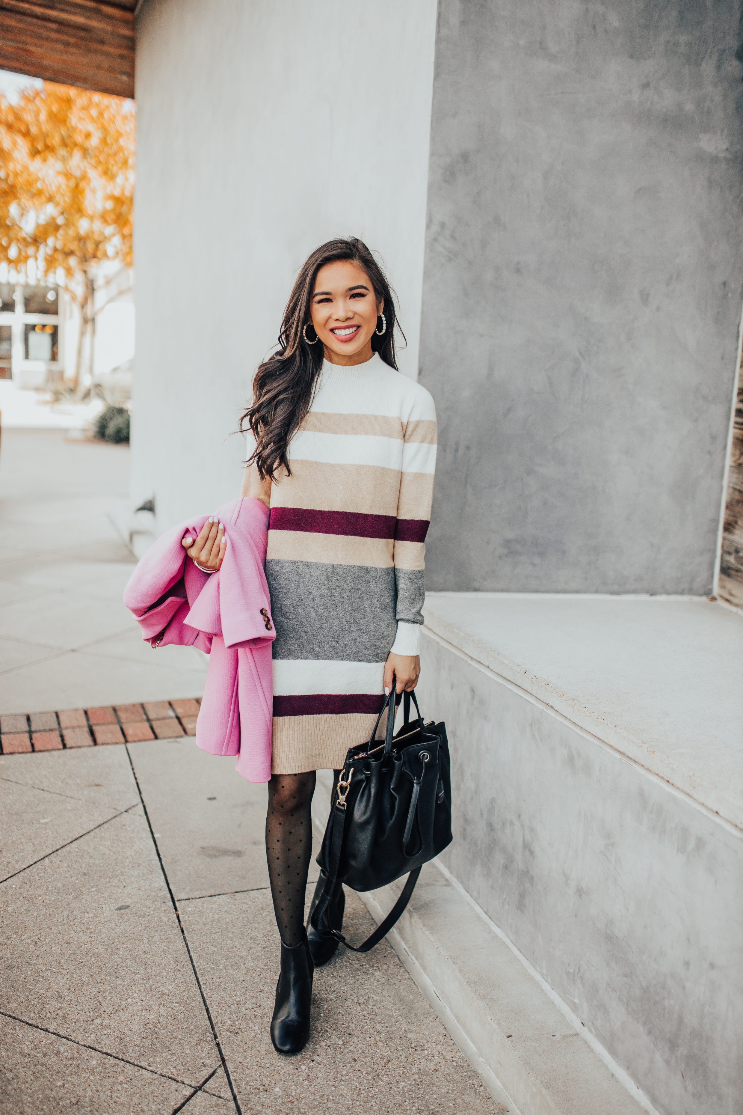 Winter workwear outfit with a striped mockneck sweater dress, pink winter coat and polka dot tights