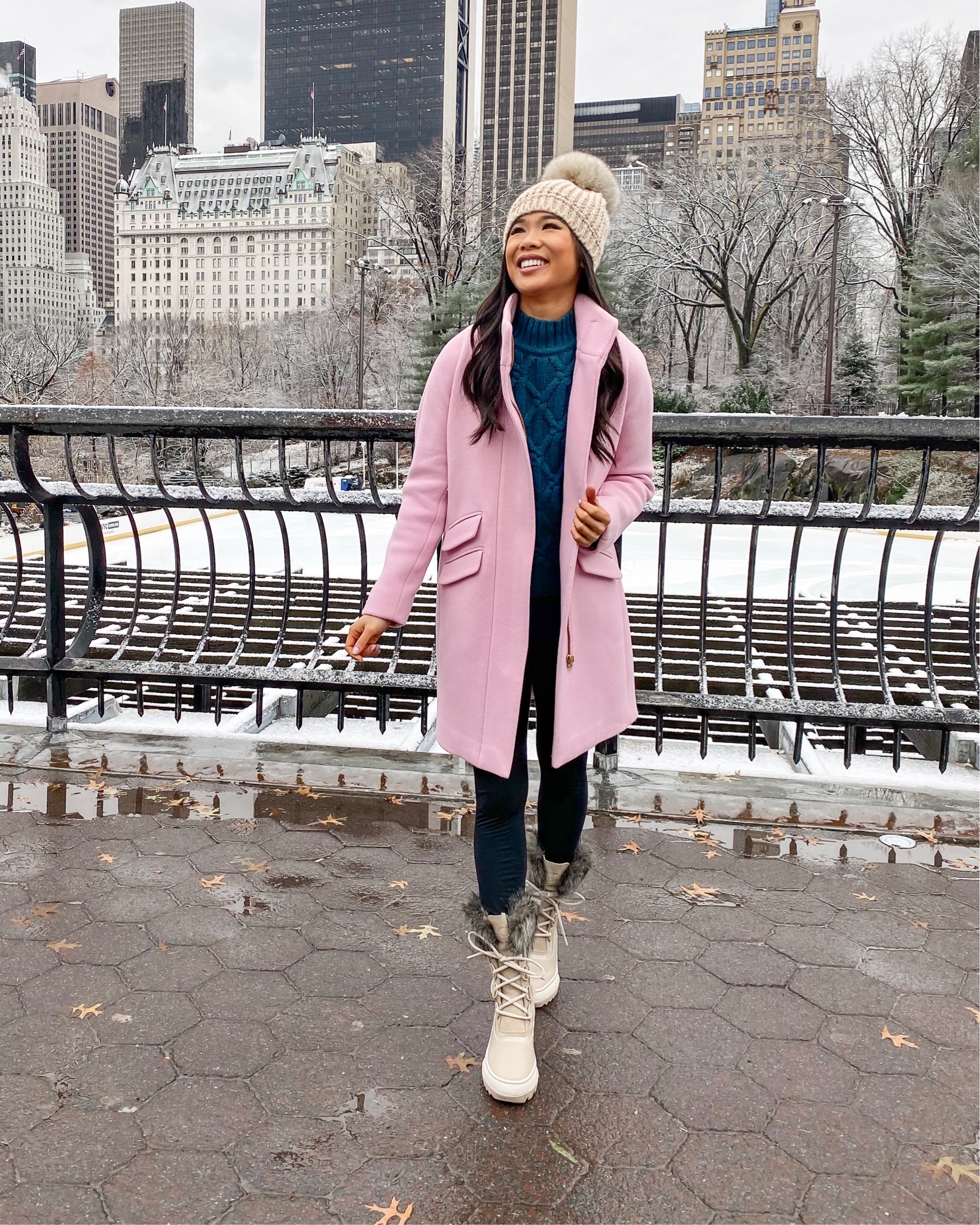 Cozy winter outfits with a pink winter coat and cream snowboots and oversized pom beanie in Central Park