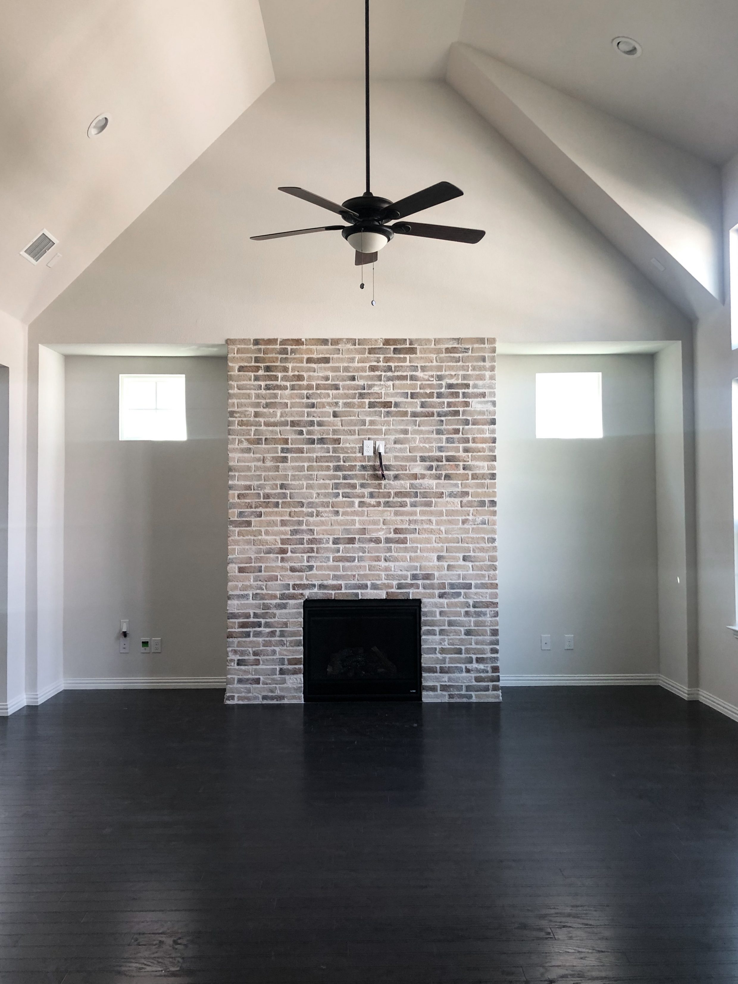High ceiling living room with brick fireplace and black fan new build house