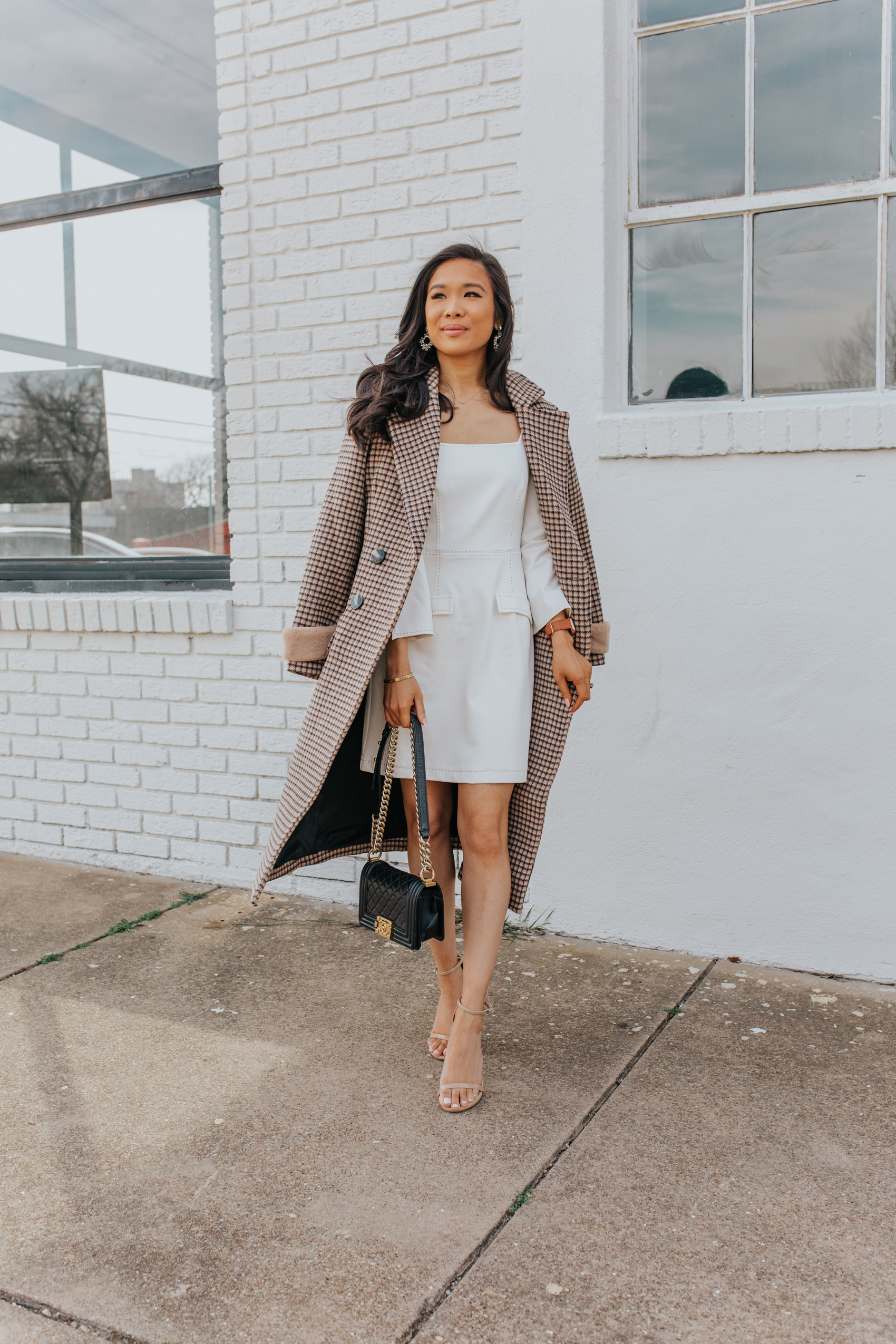 Blogger Hoang-Kim shares a winter bridal shower look with a plaid coat, white long-sleeve dress, Stuart Weitzman nudist sandals, Chanel Boy Bag and olive + piper earrings