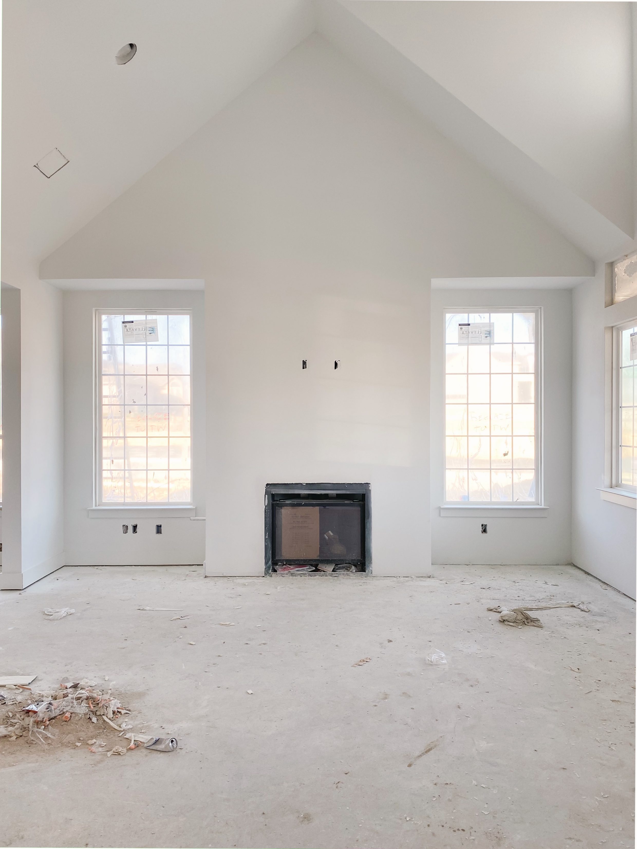 Vaulted ceilings in a living room with picture windows flanking the fire place of a one-story new build home in Dallas under construction