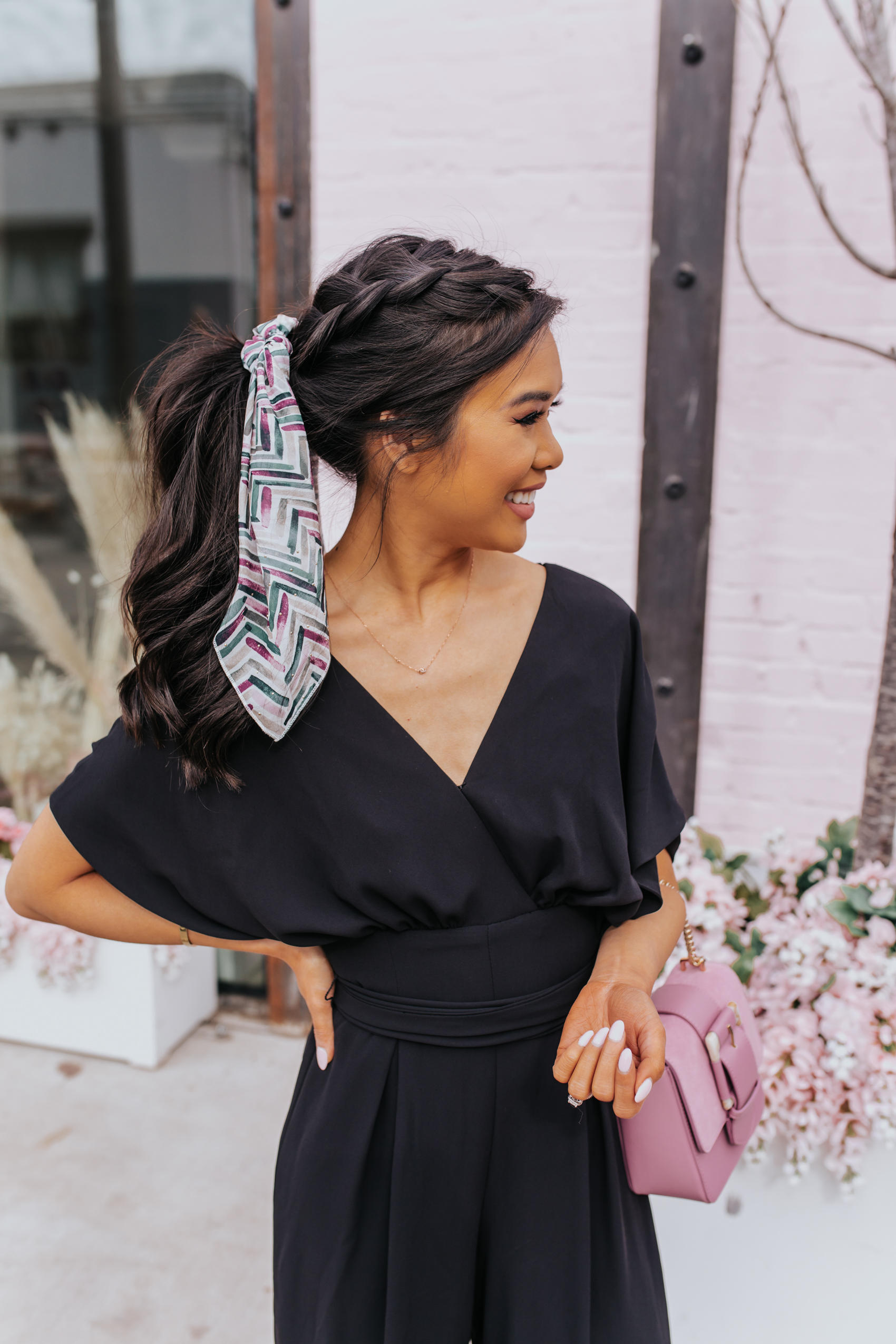 Messy braided ponytail by Tousled Studio in Dallas on petite blogger Hoang-Kim wearing a black jumpsuit, diamond Kendra Scott necklace and pink bag