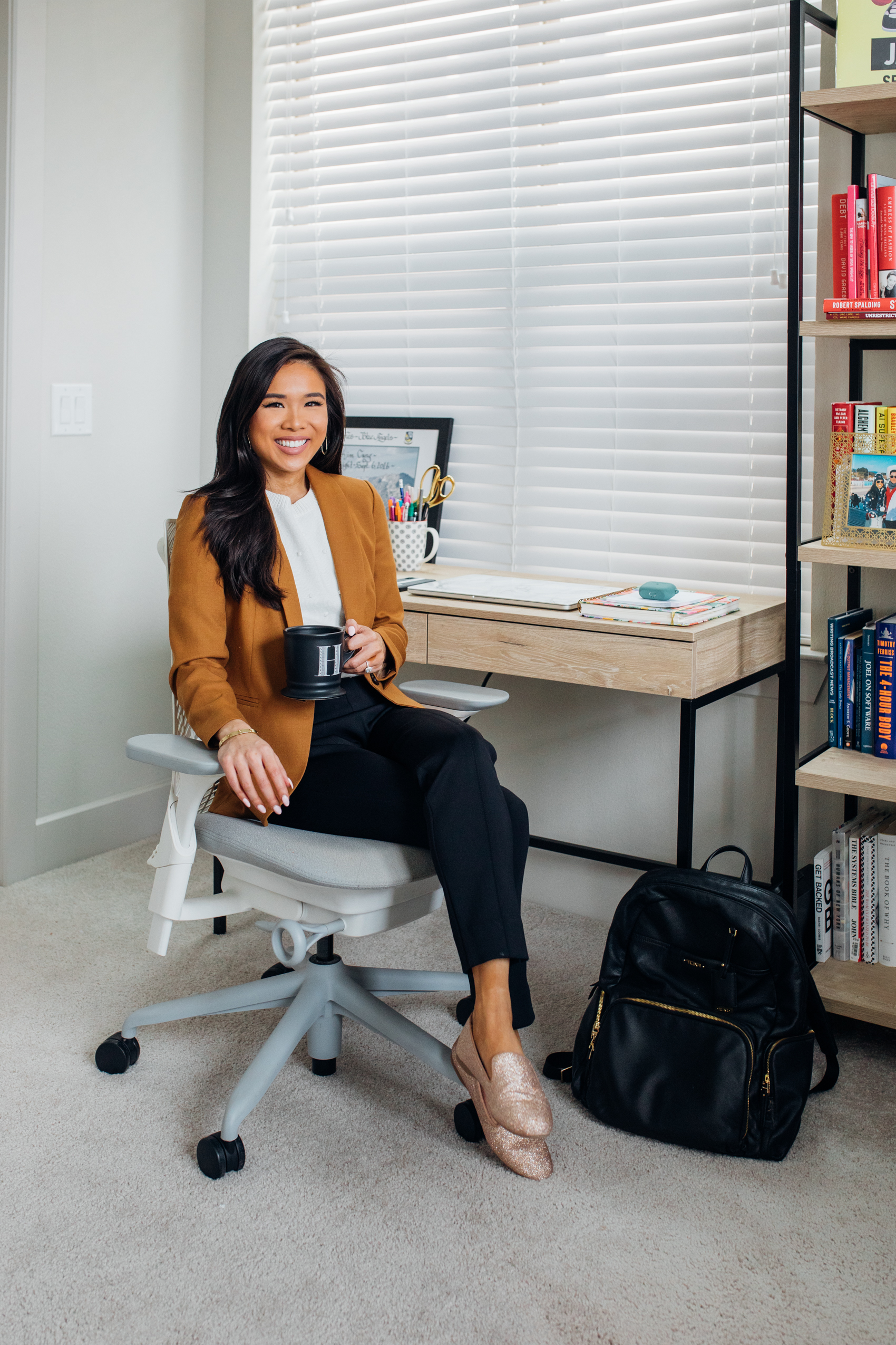 Blogger Hoang-Kim in her home office with a writing desk, Herman Miller Sayl Chair in white, Tumi leather backpack, wearing J.Crew Parke Blazer, Ann Taylor Popcorn Sweater, M.M. LaFleur Scuba Pants and Birdies flats