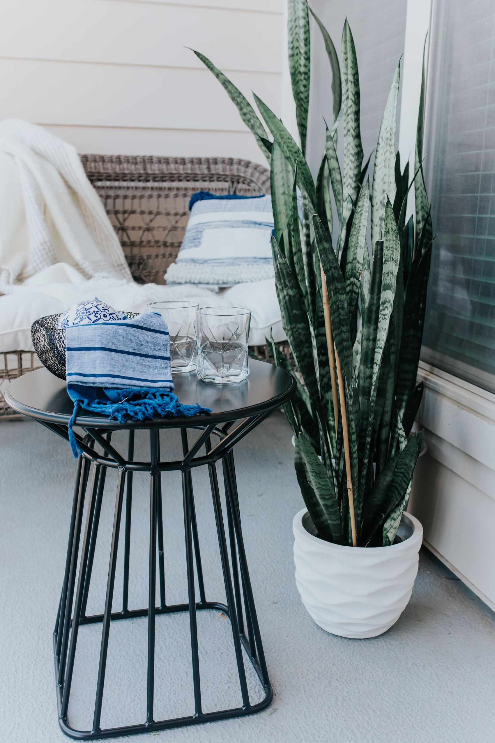 Dallas apartment balcony patio space with a gray metal table, snake plant and wicker sofa