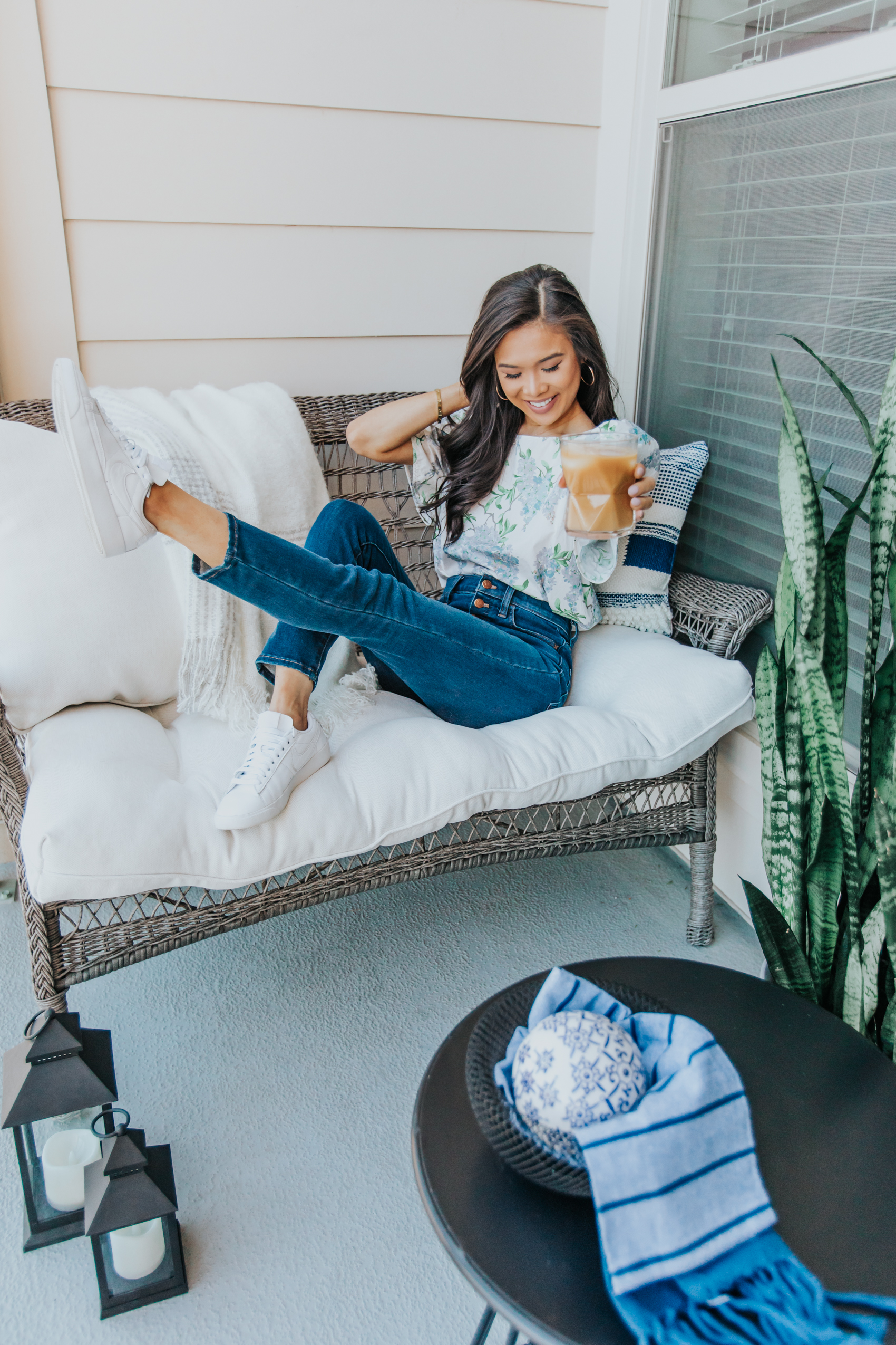 Blogger Hoang-Kim wearing a puff sleeve floral top in her small apartment patio space with a wicker sofa, cushions and lanterns