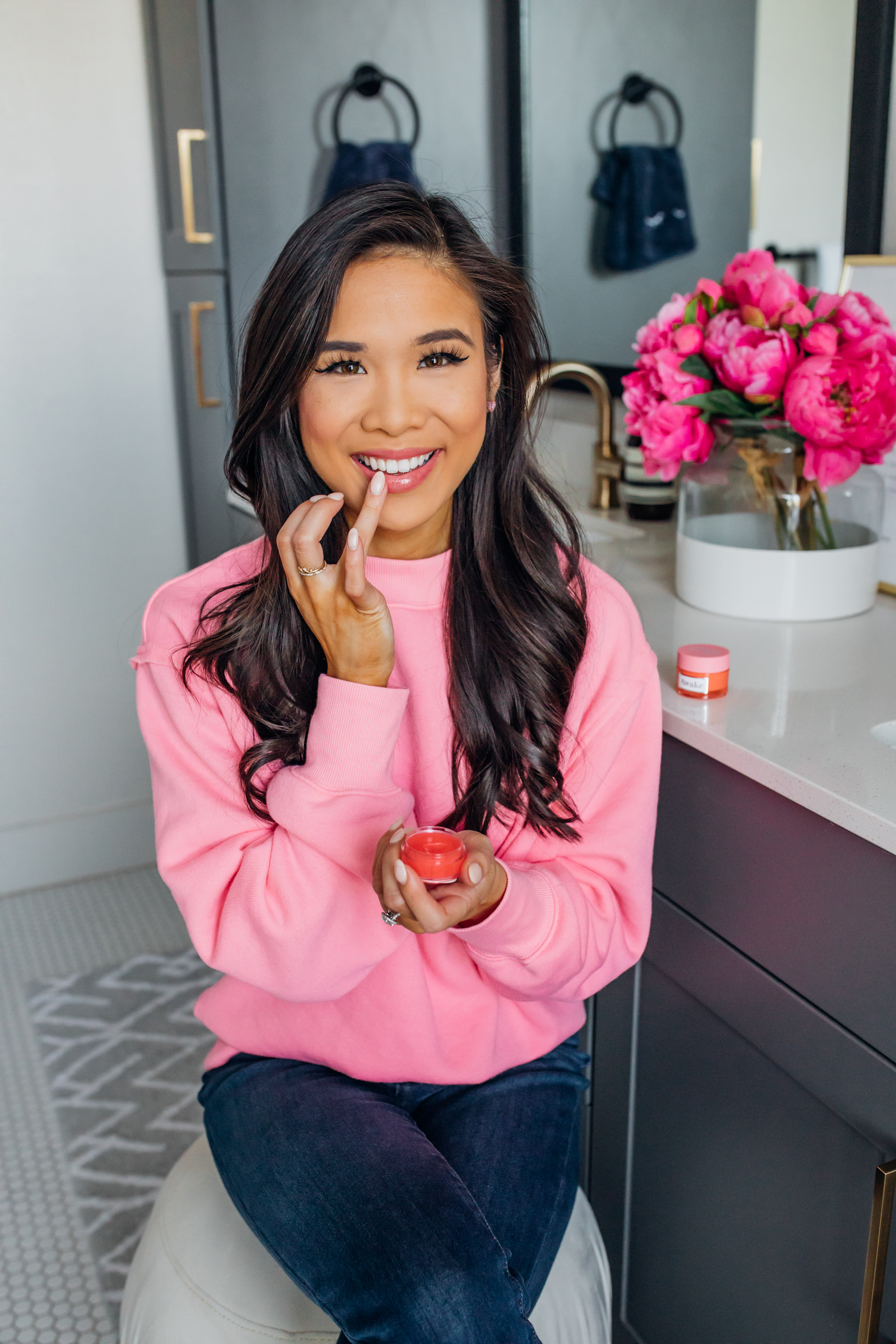 Blogger Hoang-Kim uses the Awake Beauty Moisture Balm Daytime Lip Mask in her Dallas apartment master bathroom with gold hardware wearing a pink Alo Yoga Sweatshirt
