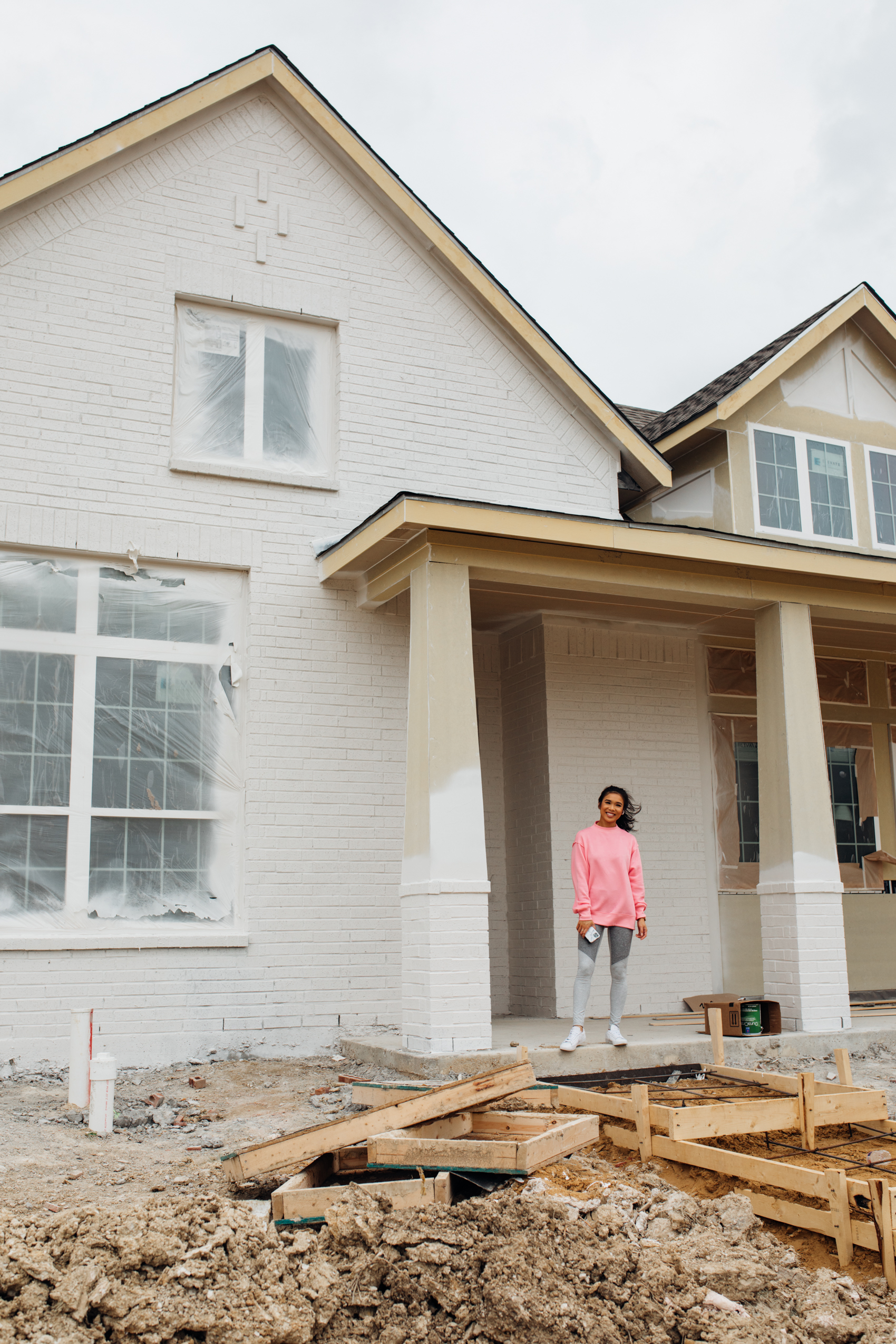 Blogger Hoang-Kim outside her white painted brick house one story floorplan currently being built in Dallas