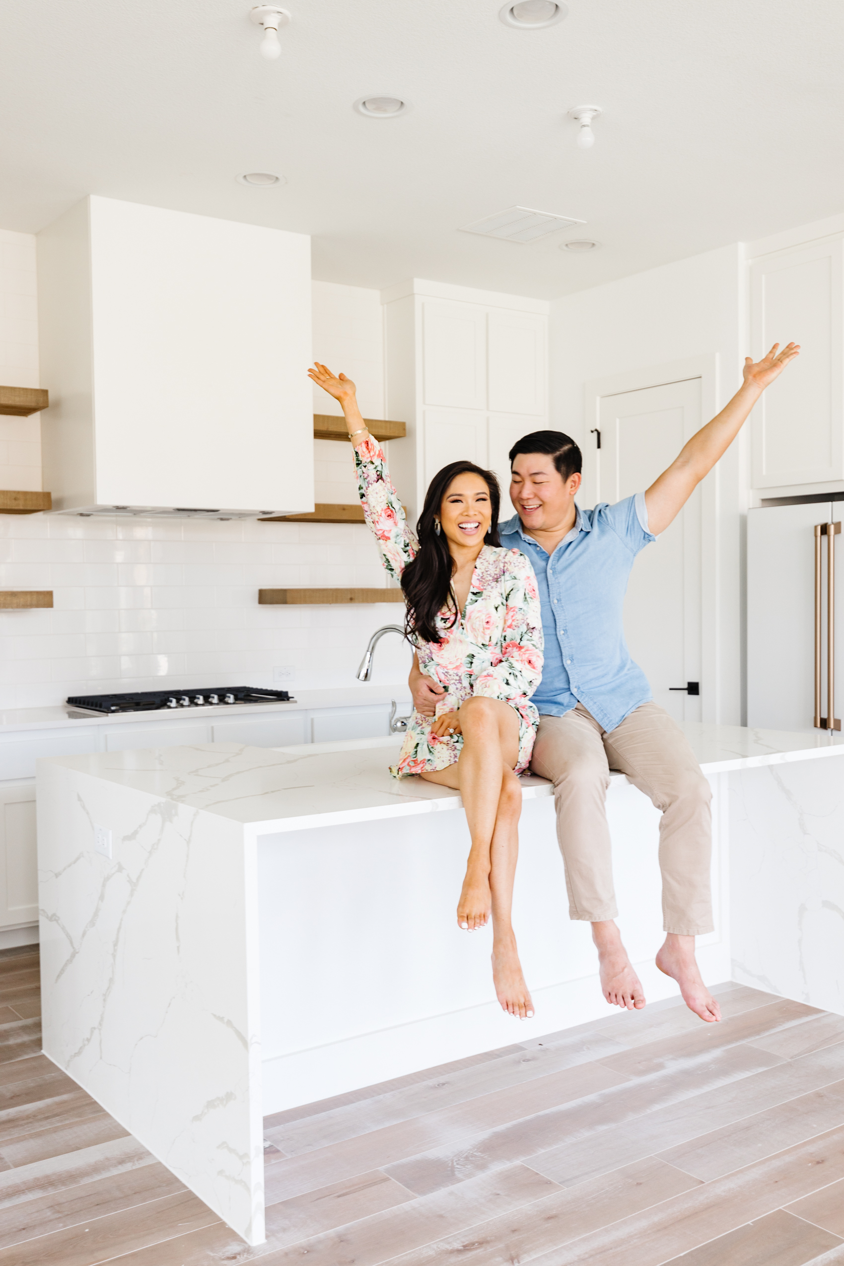 Hoang-Kim and Johnny in their new build home with a quartz waterfall island, custom range hood, open shelving and gold finishes in their kitchen