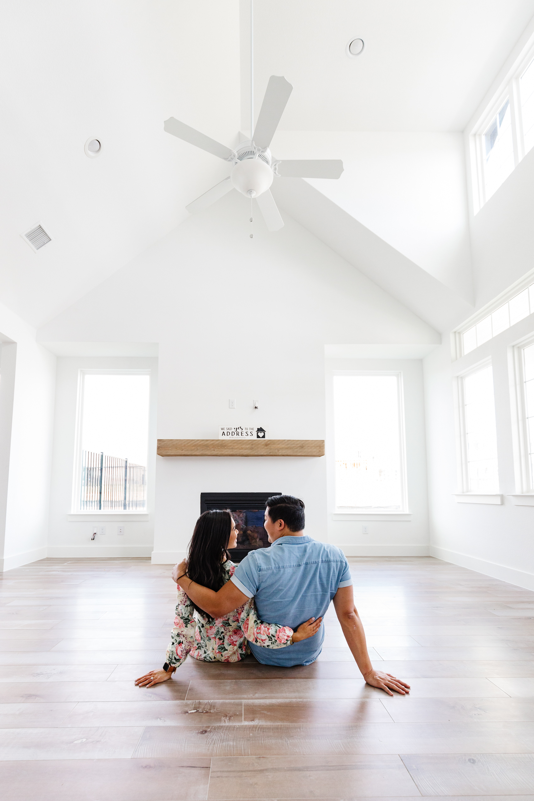 Asian couple who are first time homebuyers in their vaulted ceiling living room with lots of big windows for natural light and maple floors