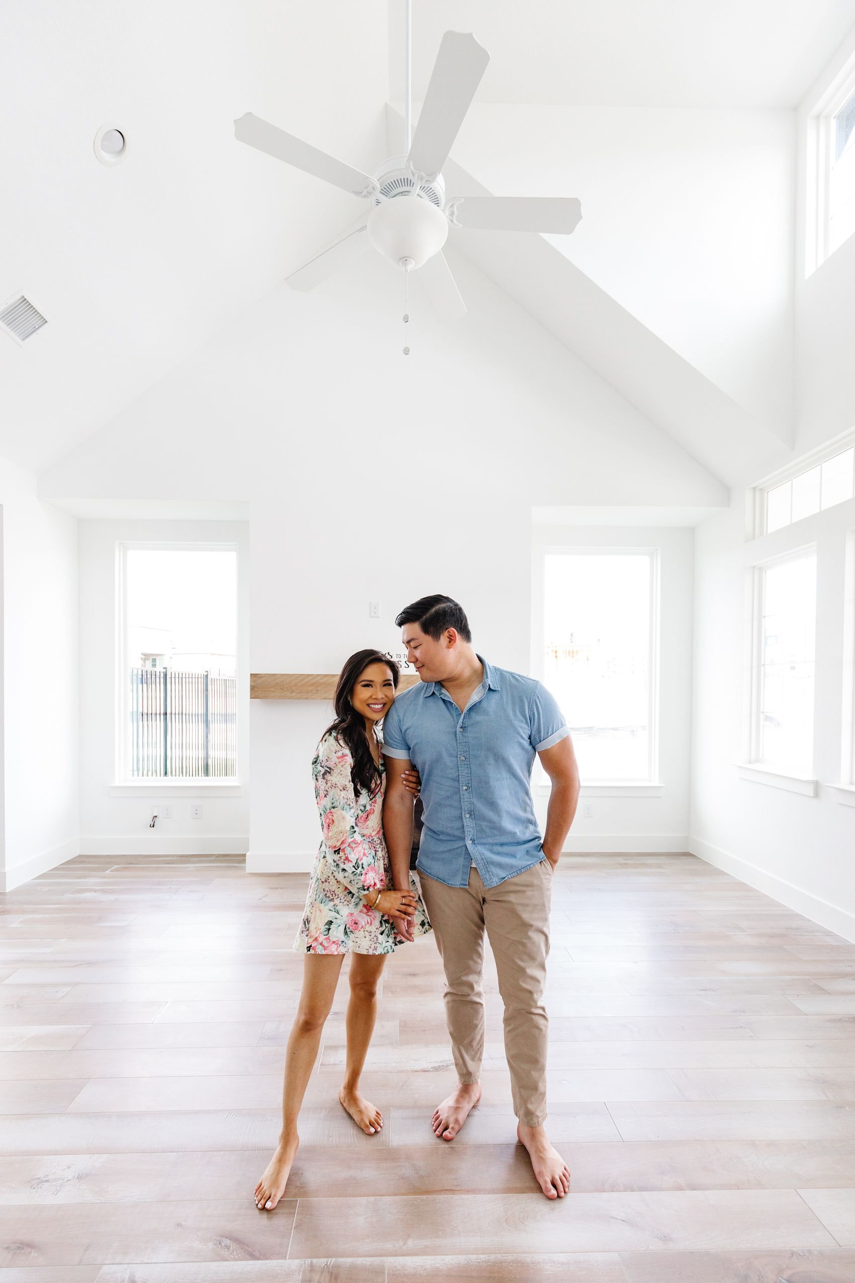Asian couple who are first time homebuyers in their vaulted ceiling living room with lots of big windows for natural light and maple floors