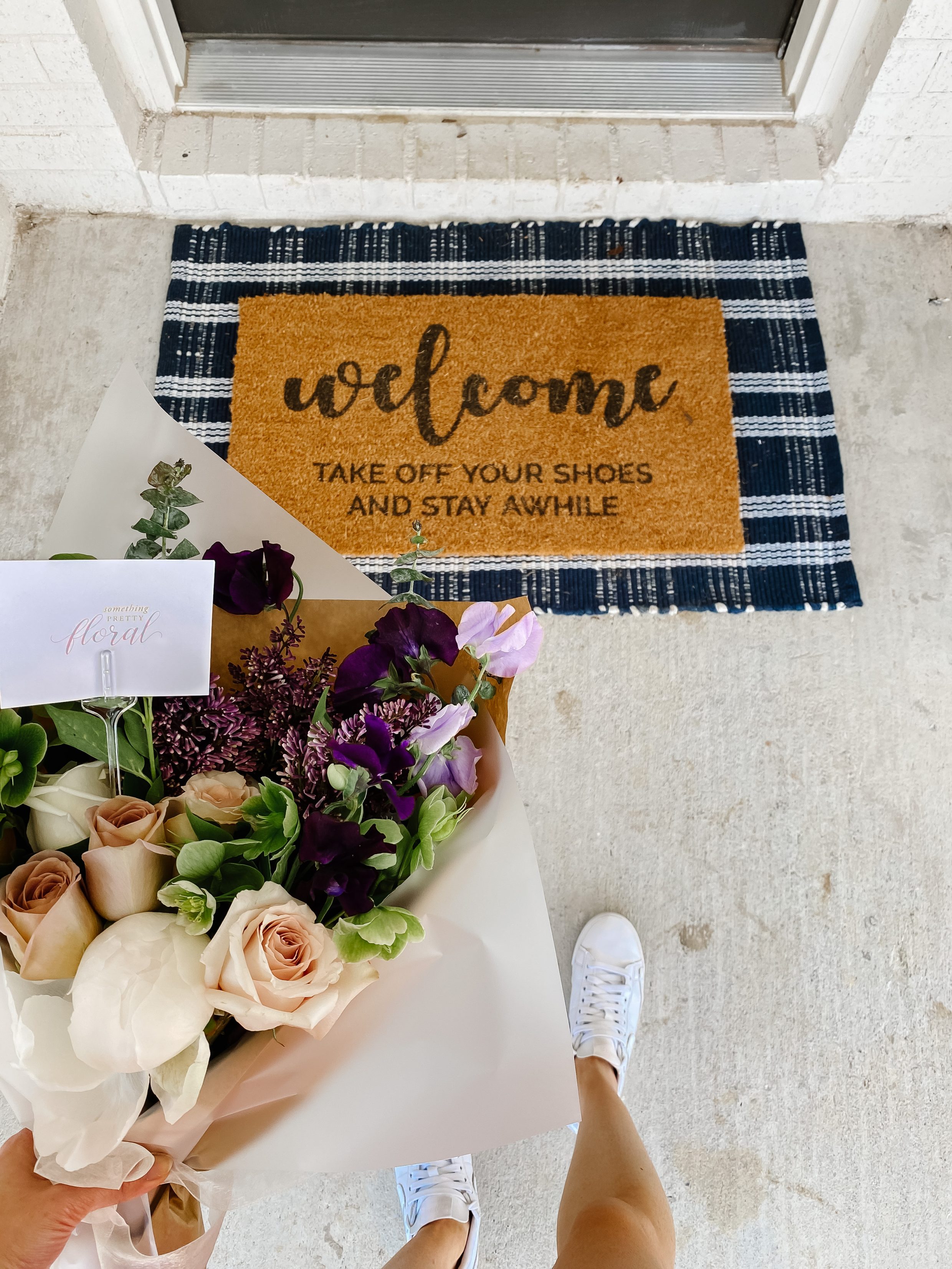 Layered door mat look with a Studio McGee Target Threshold nay plaid rug, doormat to remind guests to take off their shoes and a floral arrangement from Something Pretty Floral