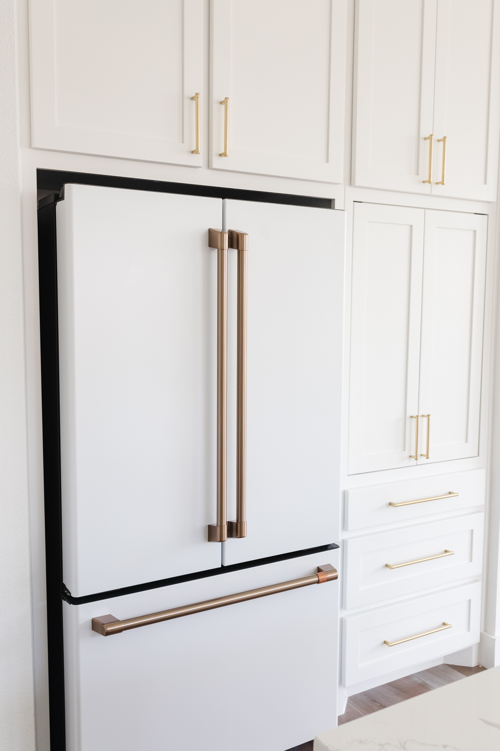 Cafe Appliances matte white refrigerator with brushed bronze handles in a white kitchen with shaker cabinets and brass hardware