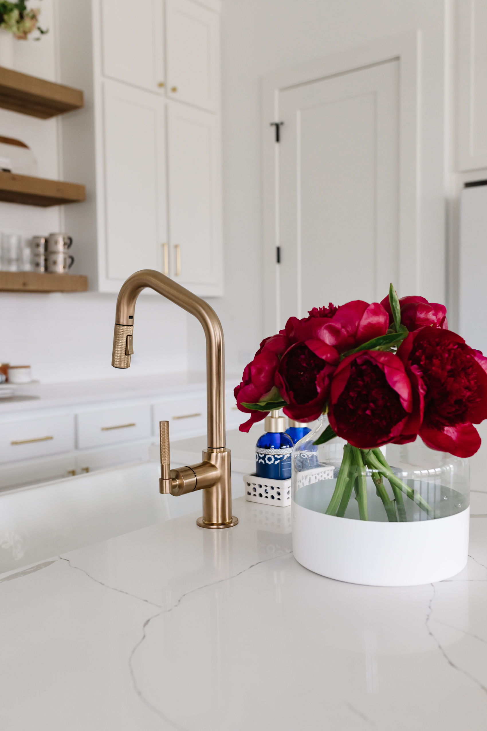 Brizo Litze Angled Pull Down faucet with knurled handle, Kohler Whitehaven farmhouse sink in a transitional kitchen with Serena and Lily Poetto vase with red peonies