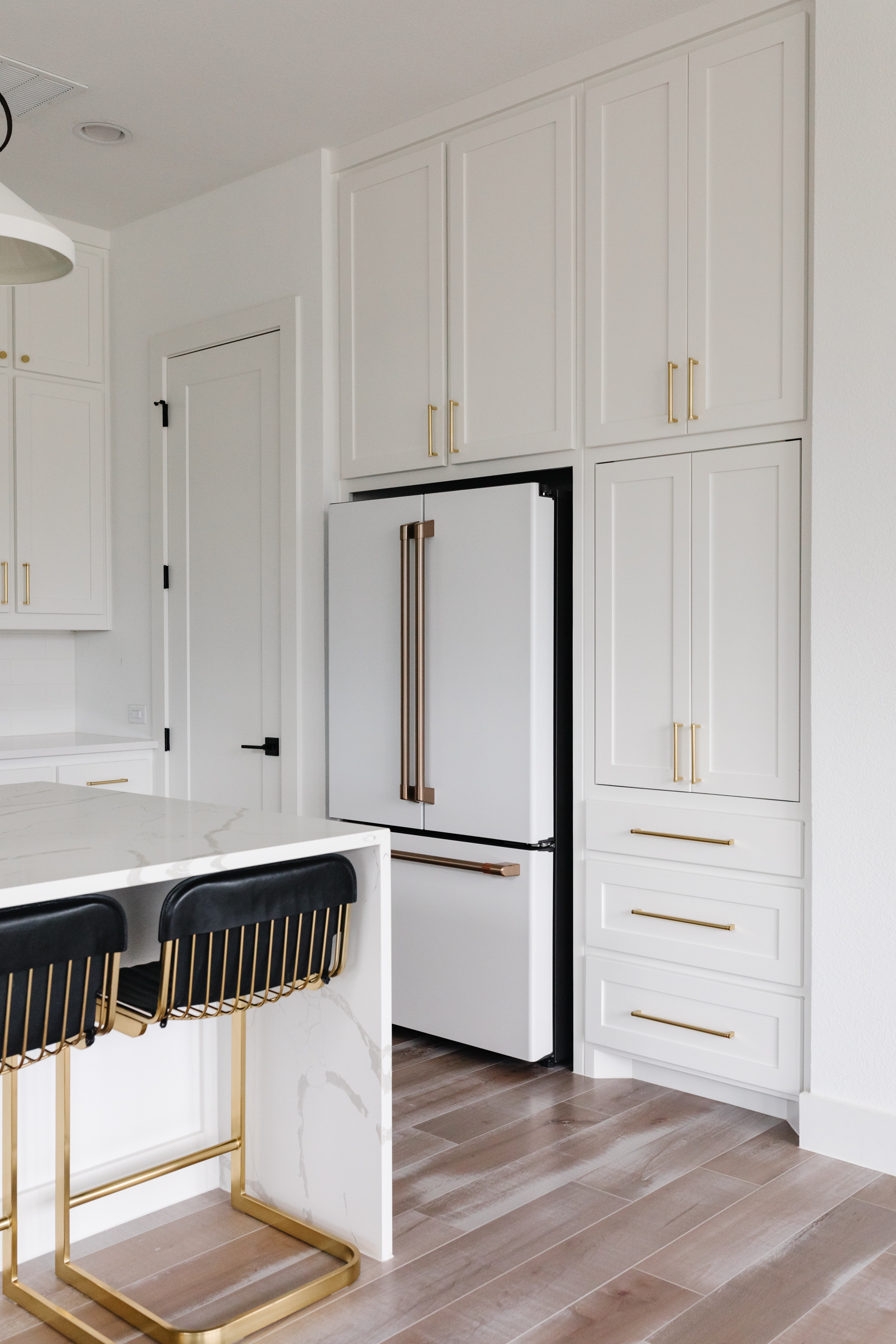 White shaker cabinets in a transitional kitchen with custom appliance garage with sliding doors, Rejuvenation hardware and calacatta foresta quartz waterfall island, Cafe Appliances refrigerator and Shaw Floors Maple Tameron Sanctuary
