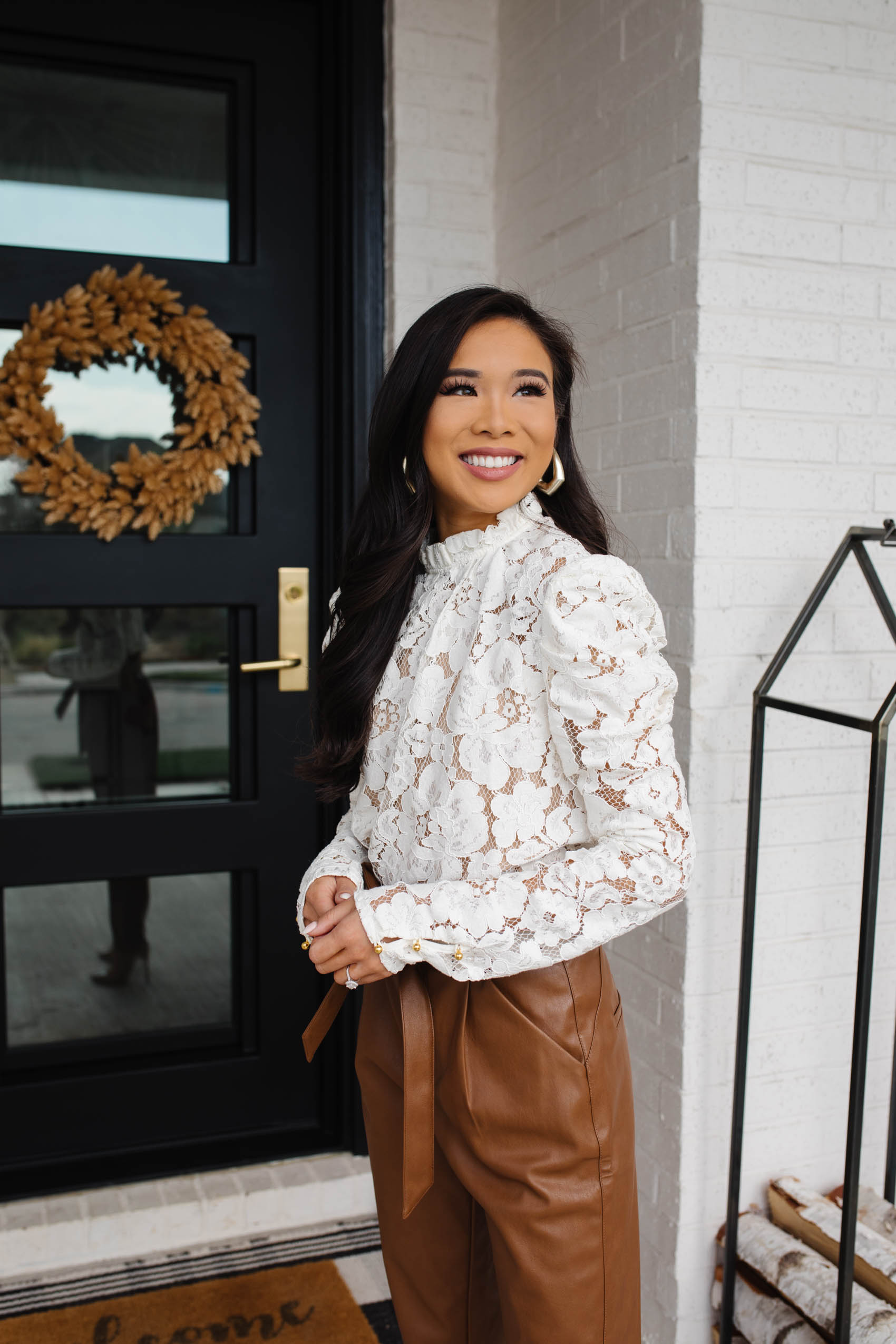 Petite blogger Hoang-Kim wears a WAYF Lace puff sleeve top and brown tie waist leather pants on her front porch