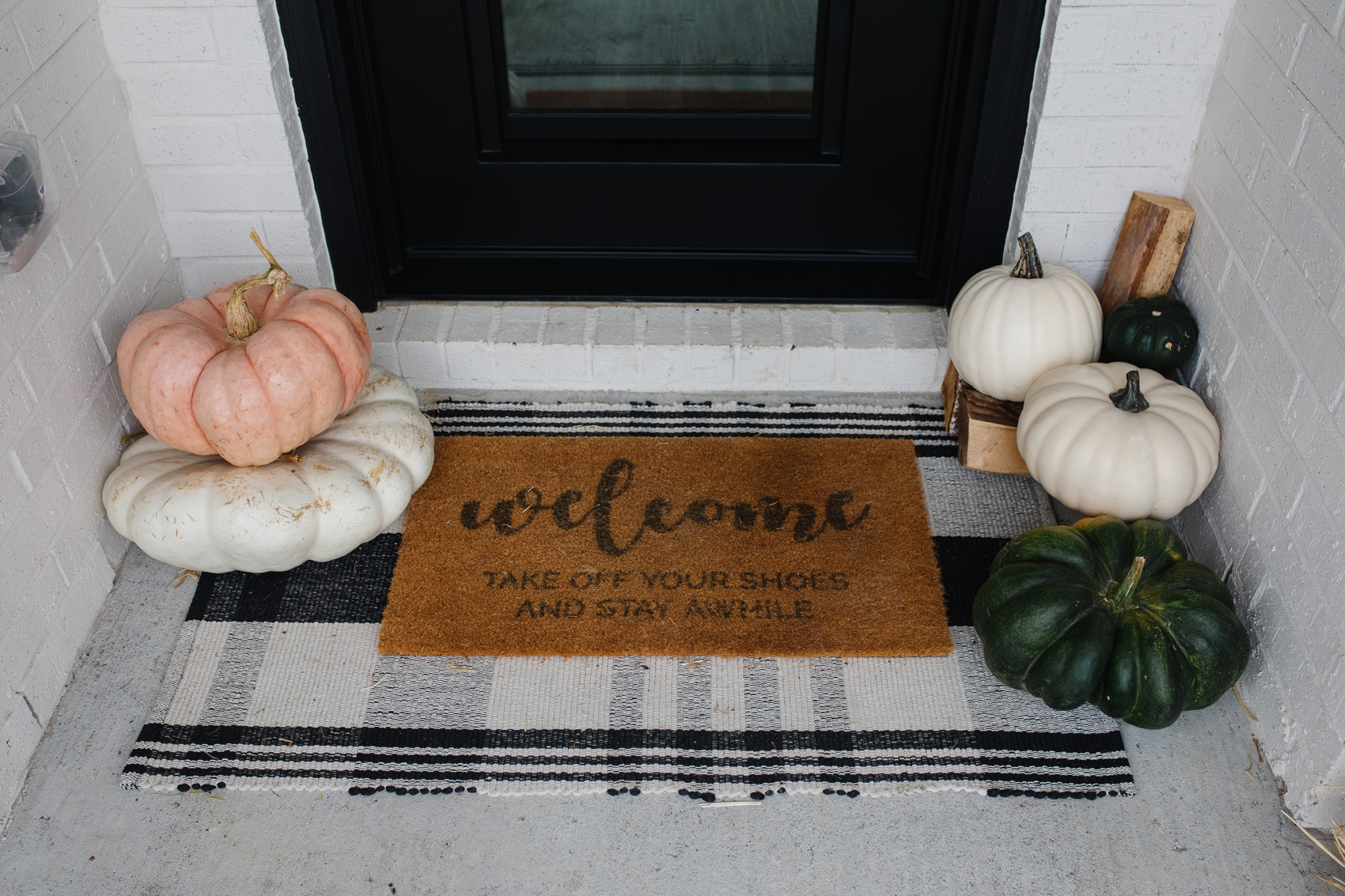 Fall front porch decor with a tartan rug, neutral pumpkins and doormat