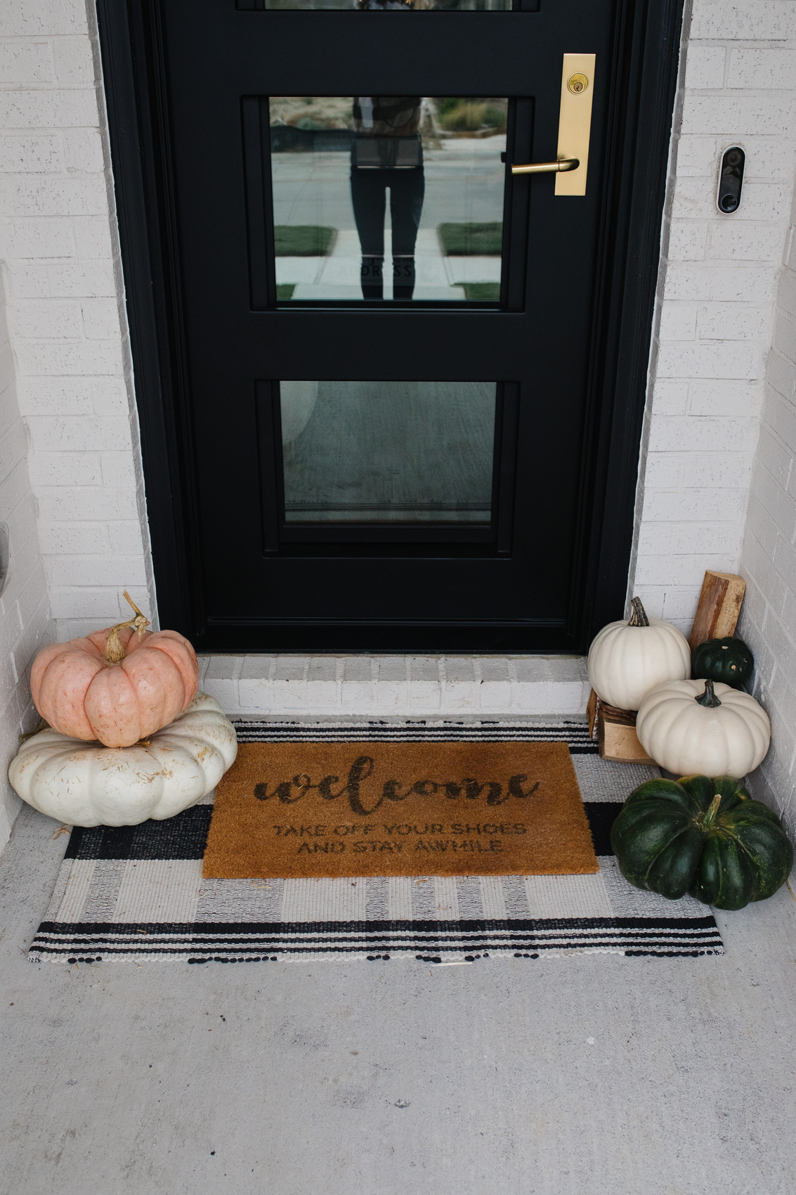 Fall front porch decor with a tartan rug, neutral pumpkins and doormat
