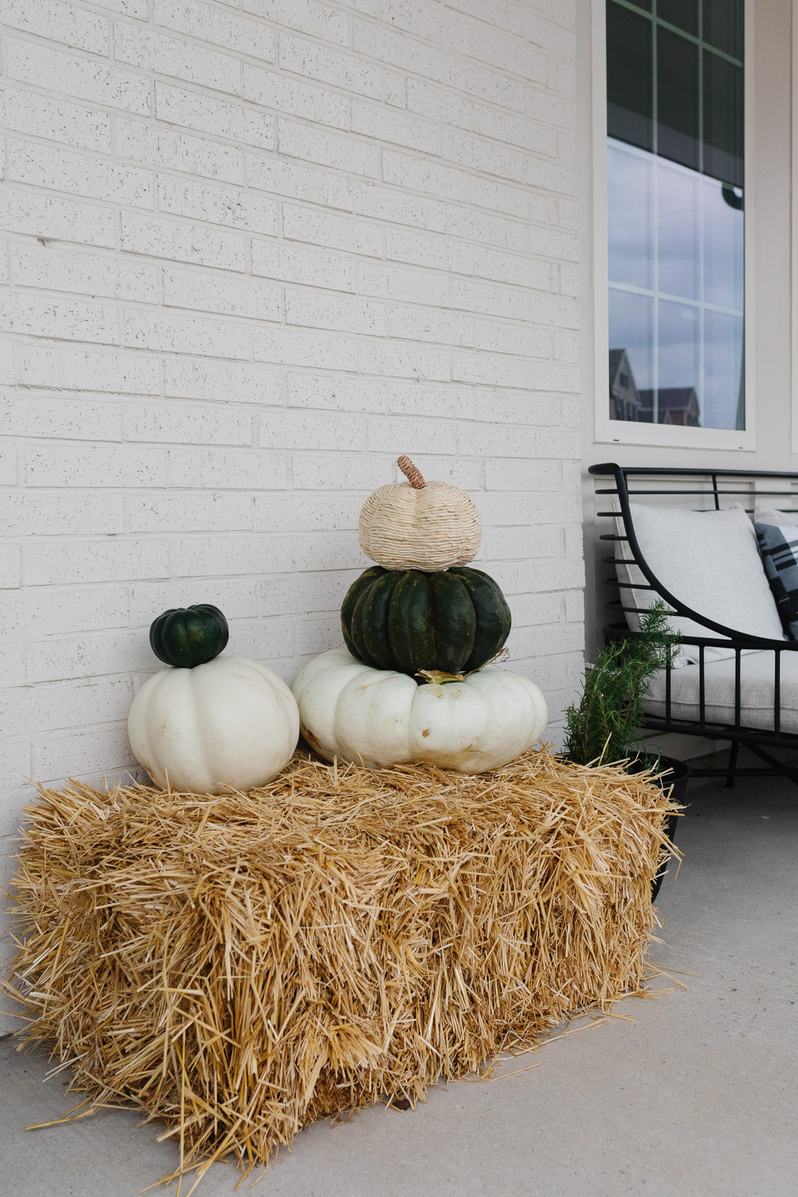 Fall front porch decor with a hay bale, white and green pumpkins, CB2 Breton sofa and plaid pillows