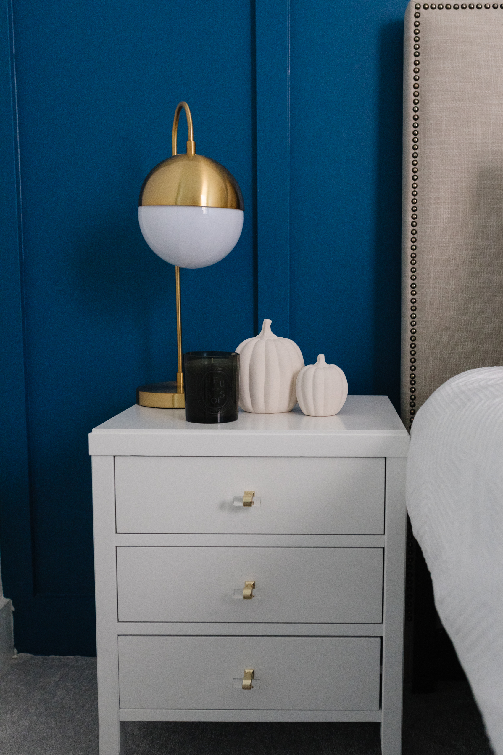 White pumpkins, white nightstand, gold globe lamp in a board and batten room