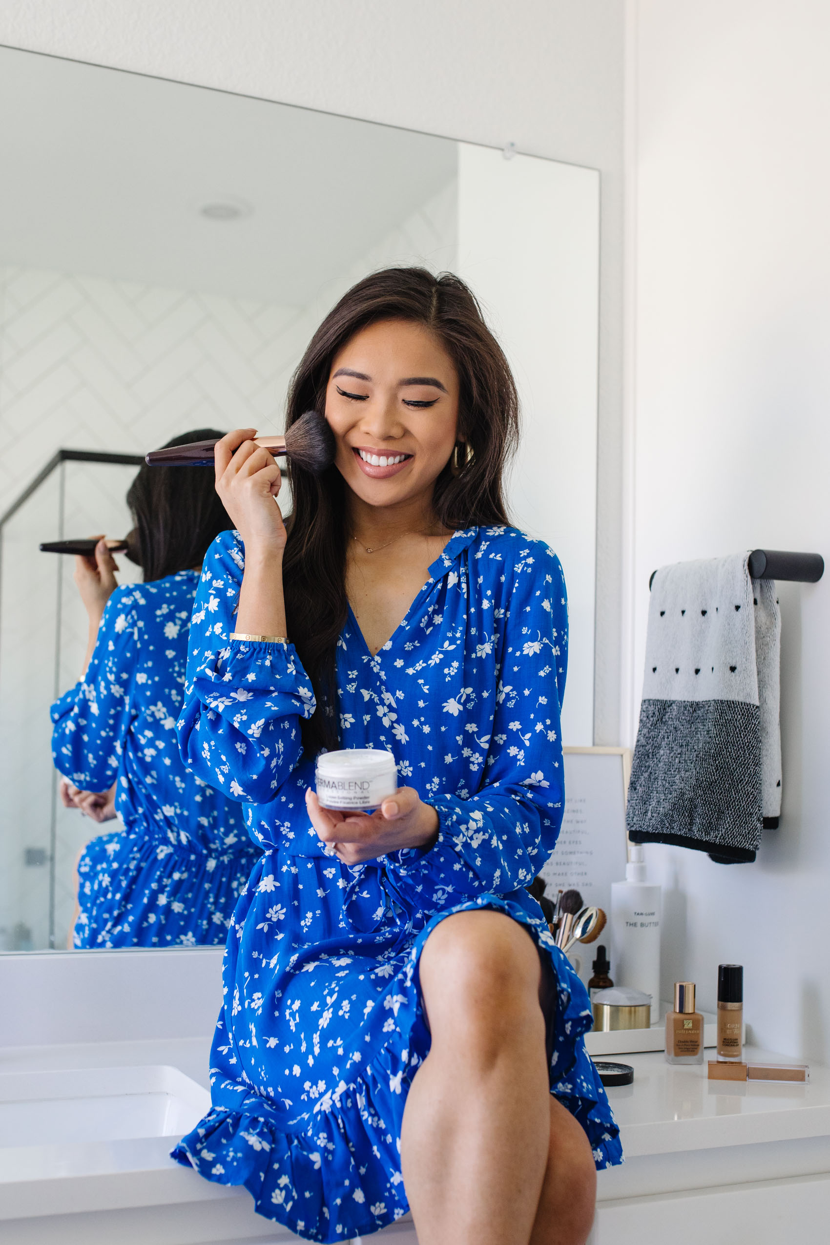 Blogger Hoang-Kim applies Dermablend loose setting powder to set her makeup in her bathroom wearing a Draper James floral dress