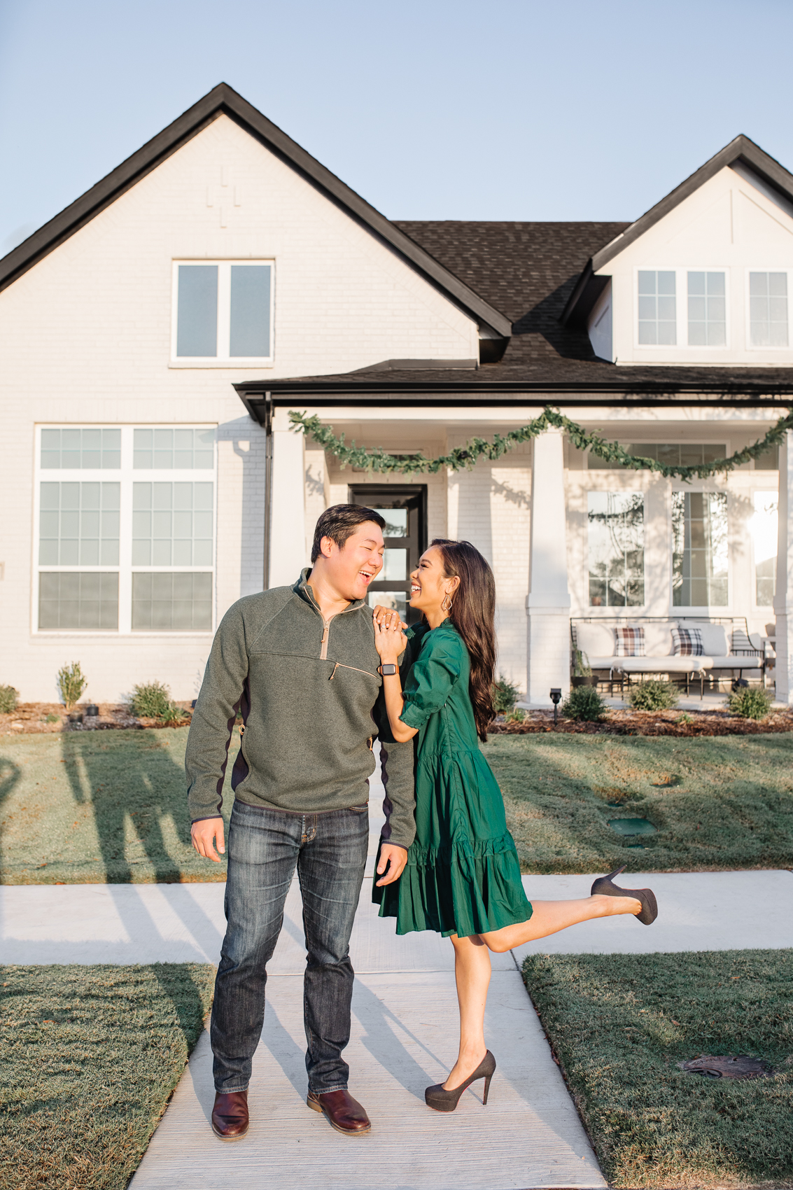Blogger Hoang-Kim with her fiancé Jonathan in front of their white painted brick house in Dallas wearing a green dress and sweater