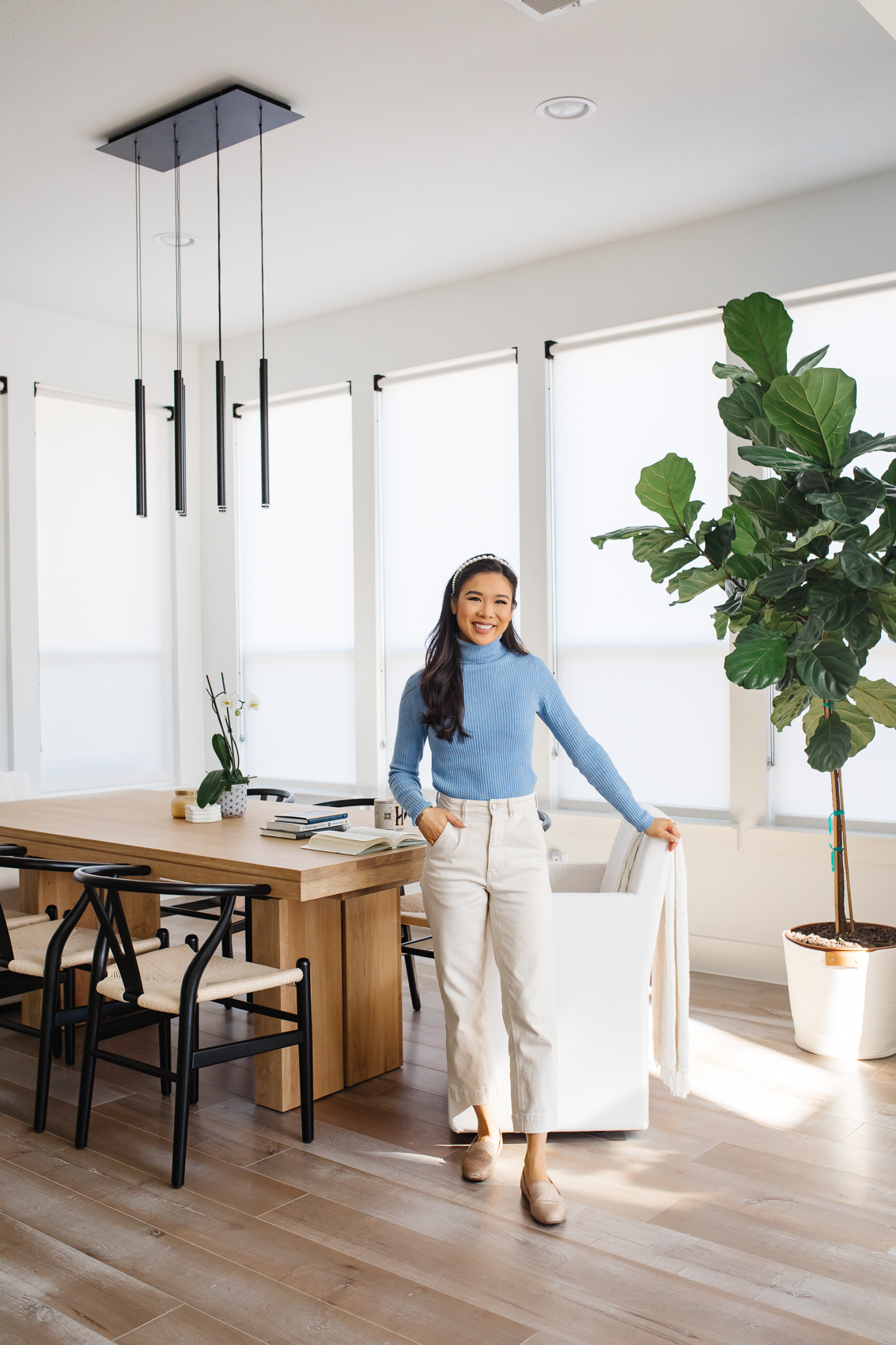 Blogger Hoang-Kim Cung in her dining room with an Ellison Track Armchair, McGee & Co Antoni extendable dining table, wishbone chairs from poly & bark, live fiddle leaf fig plant, modern LED chandelier with inspiring books