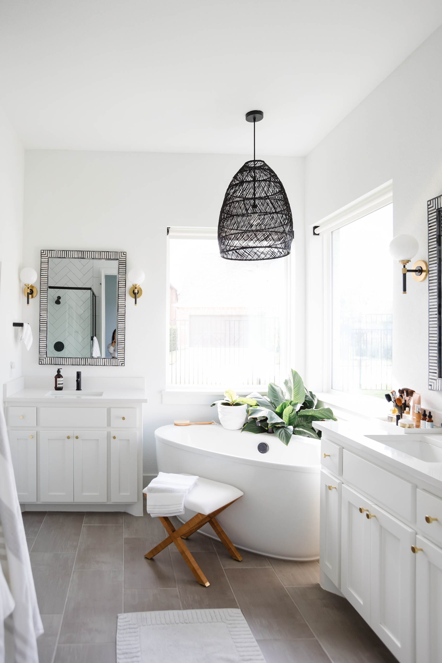 Blogger Hoang-Kim Cung's white transitional bathroom with luxury bathroom accessories like a Serena & Lily pendant, Bar Harbor Mirrors, Hudson Valley Lighting Bowery sconces, balboa X stool and more