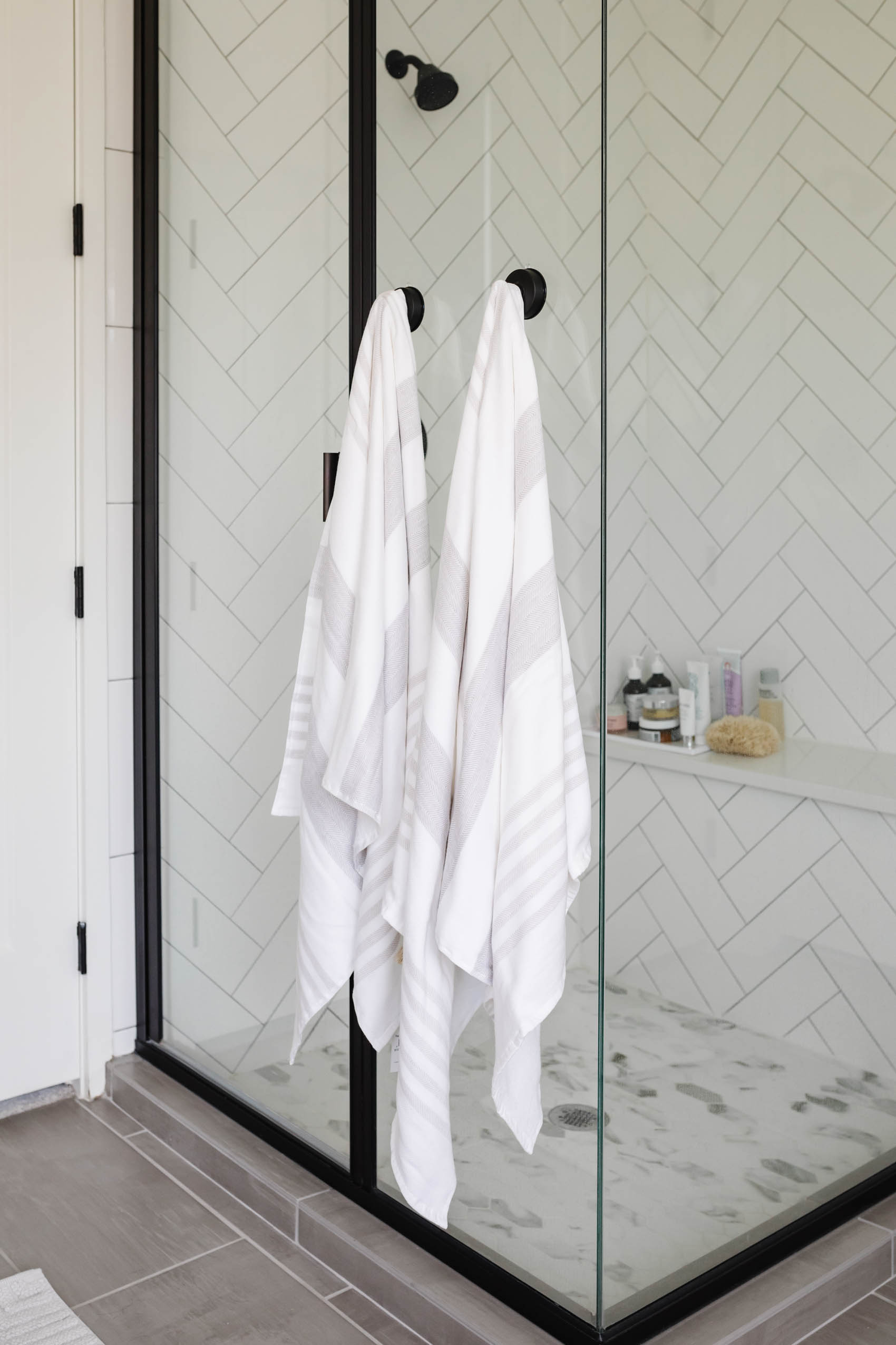 luxury bathroom accessories including Serena & Lily Fouta Bath Towels on white herringbone shower tile