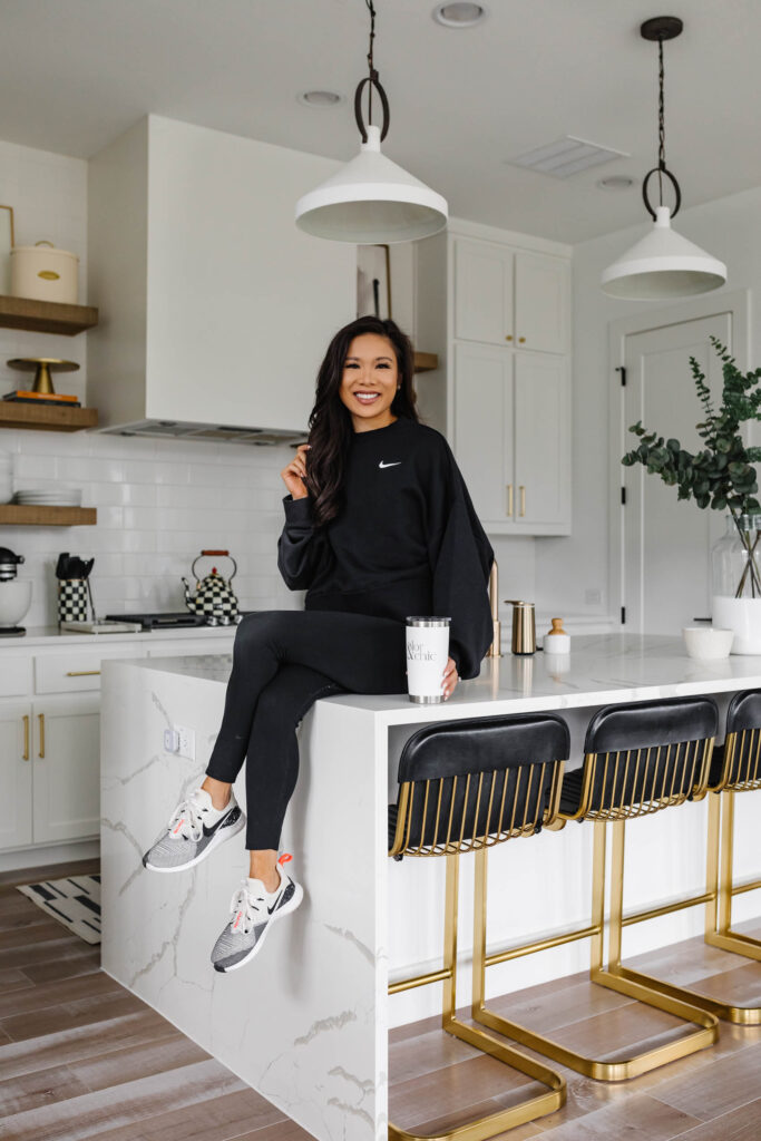 Blogger Hoang-Kim Cung wears a nike sweatshirt and nike one lux 7/8 leggings in her white kitchen