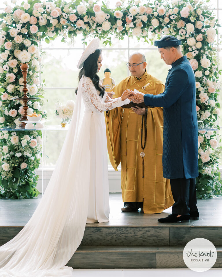 Hoang-Kim and Jonathan Van at their Buddhist wedding ceremony wearing Vietnamese ao dai under a floral arch