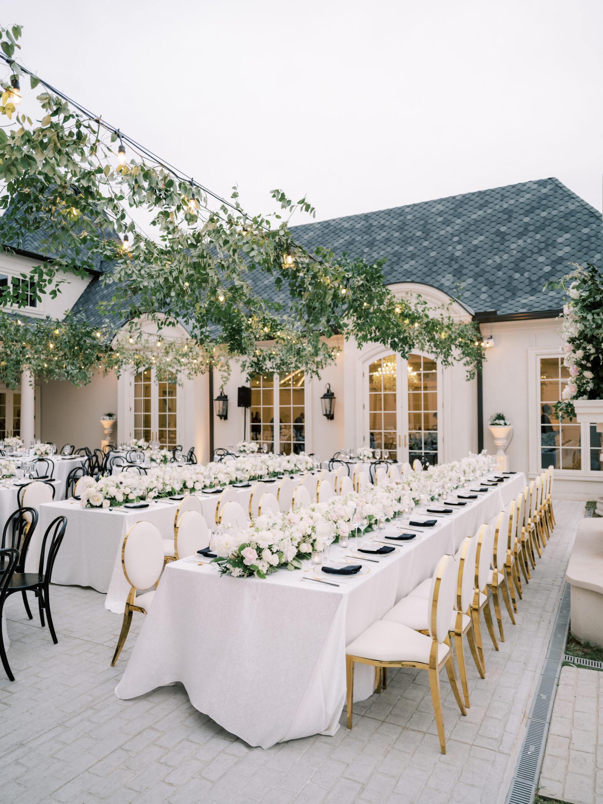 Outdoor wedding reception with hanging greenery, gold and white dining chairs, lush florals by Something Pretty Floral, black bistro chairs at Dallas wedding venue The Hillside Estate