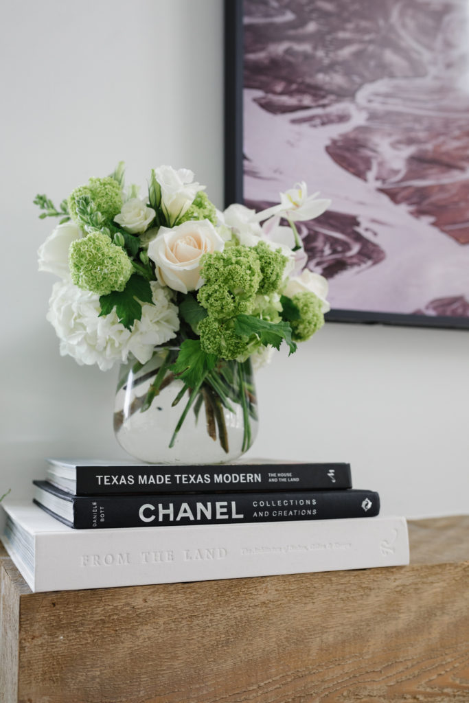 White and green floral arrangement on top of Texas Made Modern, Chanel and From the Land coffee table books on a floating mantel.