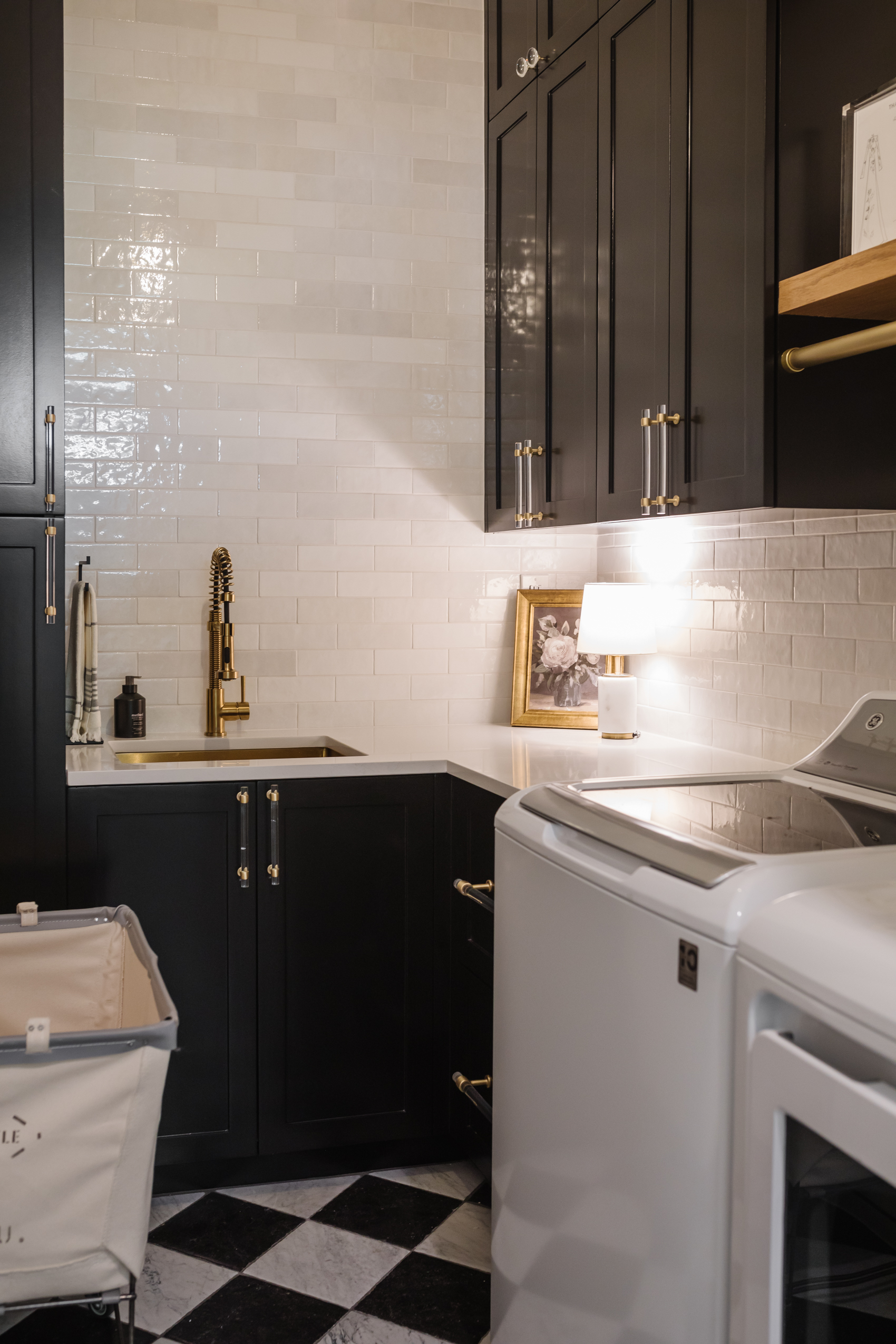 Laundry room with tricorn black cabinets, marble checkerboard floors, Alexander James Tile studio subway tile backsplash and a brass sink.
