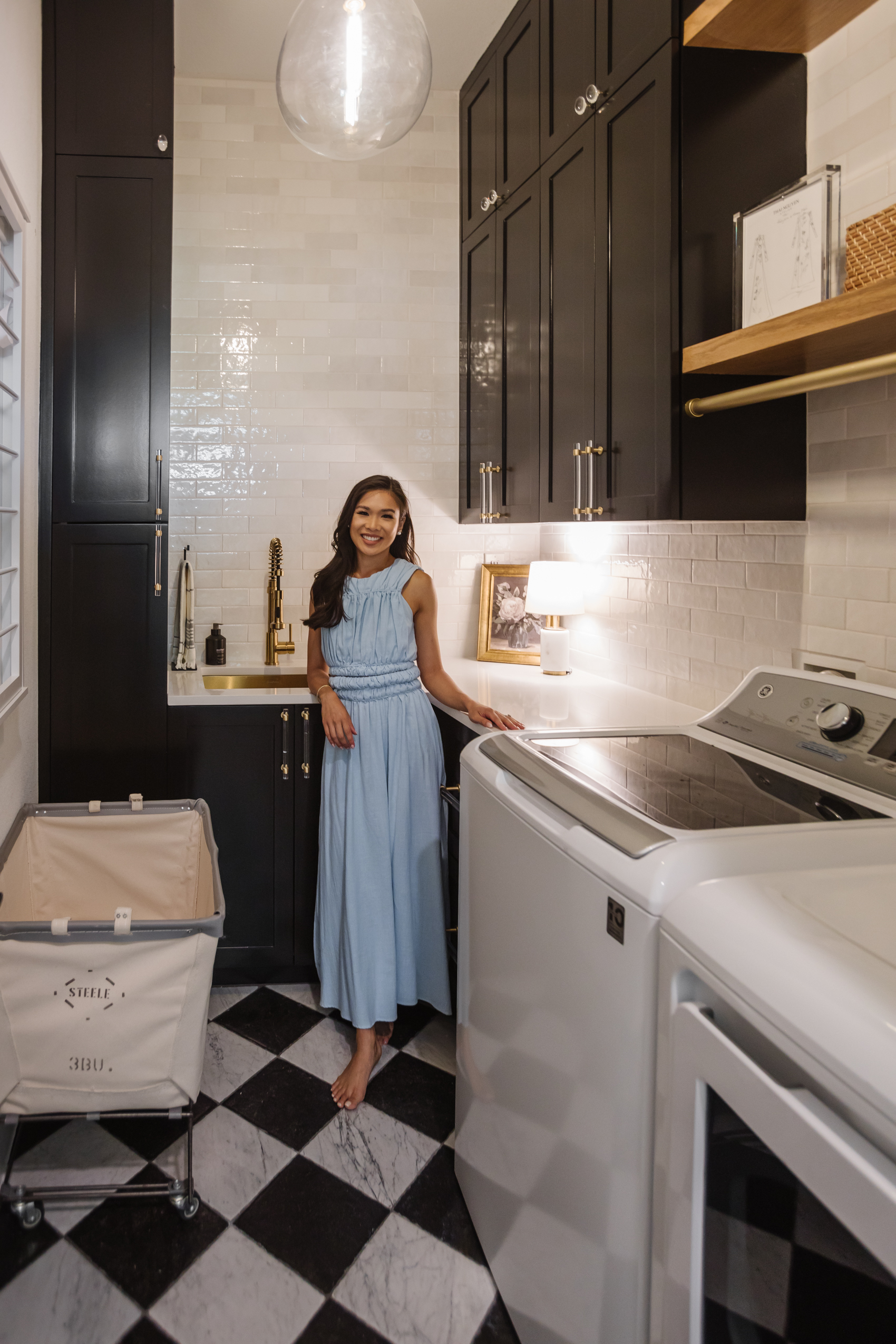 Blogger Hoang-Kim in her laundry room with marble checkerboard floors, subway tile backsplash, Hudson Valley Ivy pendant and custom cabinets