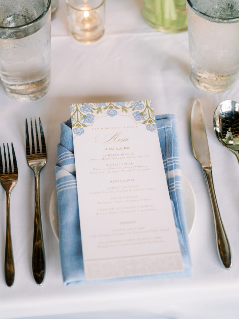 Blue rehearsal dinner table setting with blue botanical menus from the knot, white place setting and silver flatware at Lounge 31 in Highland Park Village
