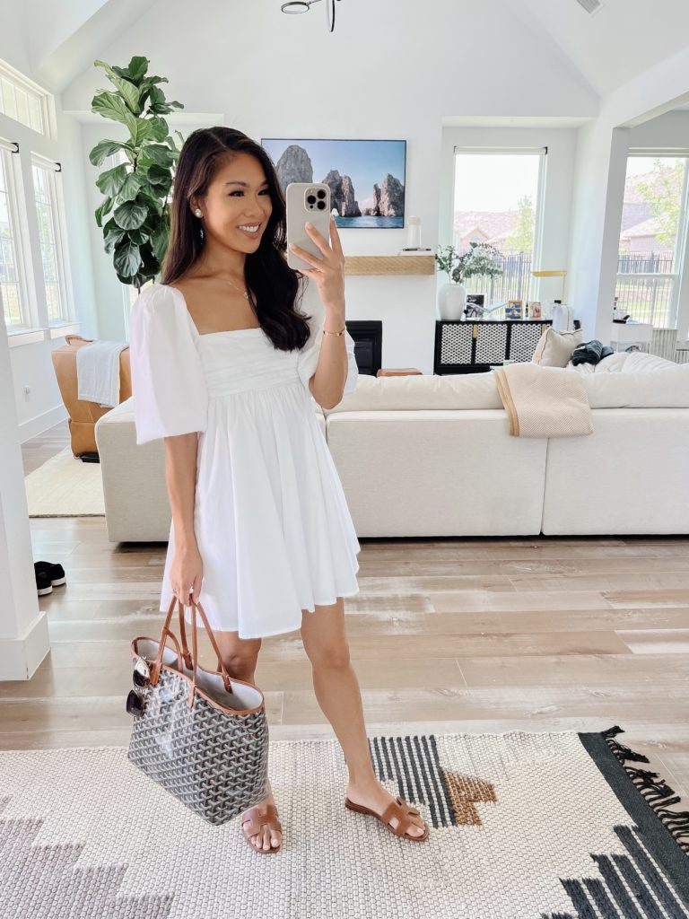 Blogger Hoang-Kim wearing a white puff sleeve Abercrombie dress and carrying a Goyard St Louis PM tote with Hermes Oran sandals.